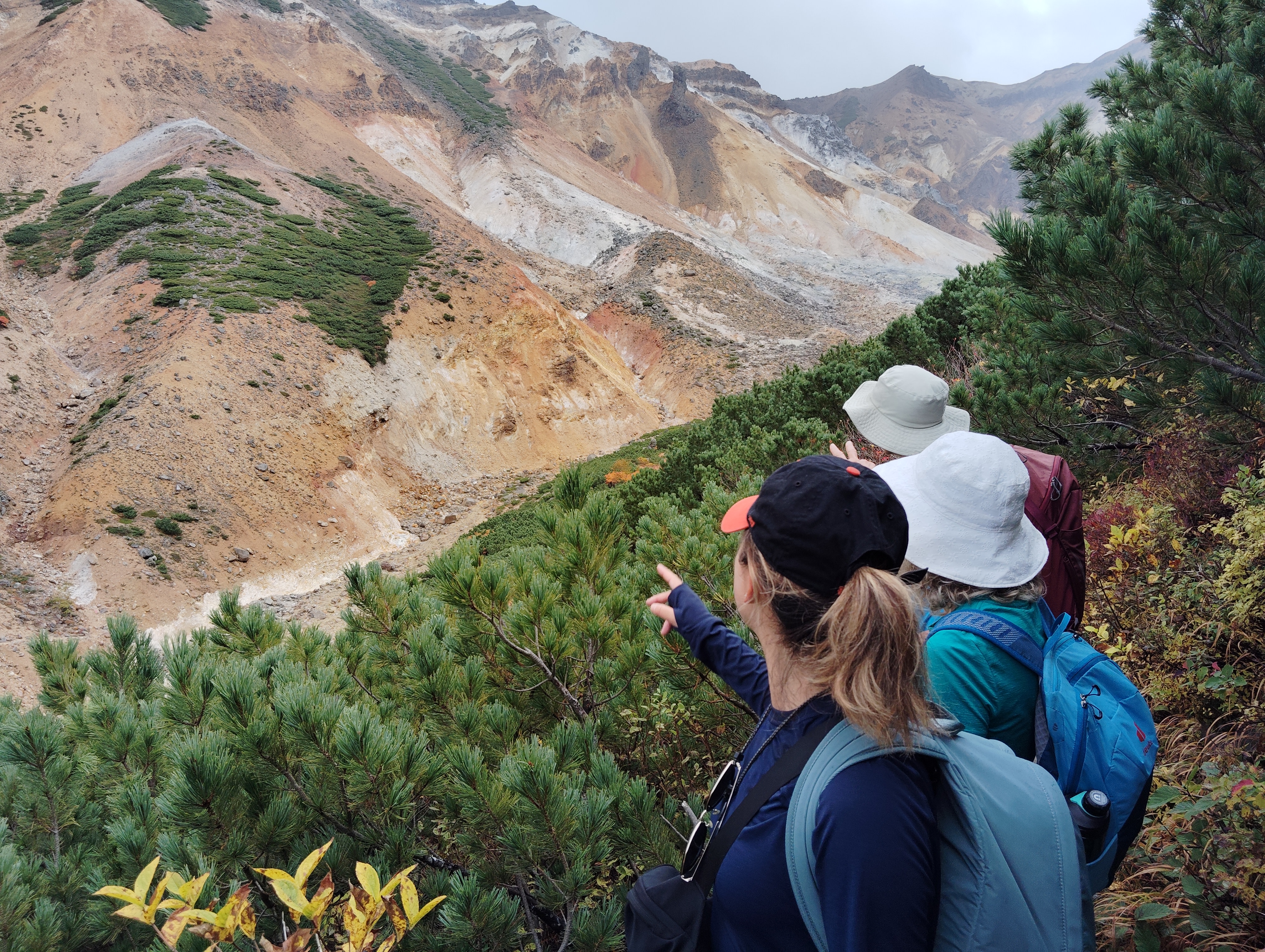 Three guests on a hiking trail point to a sandy and rocky valley below.