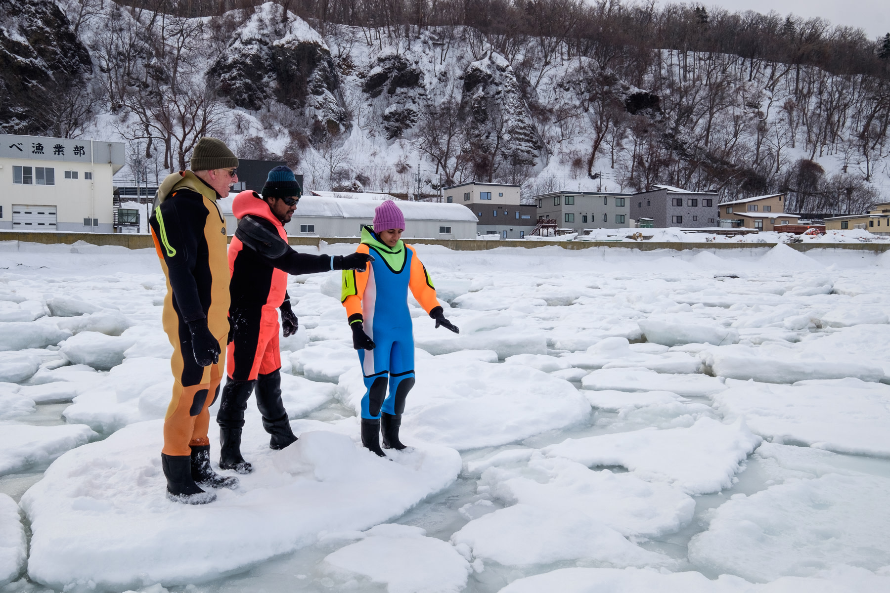 A group of people wearing dry suits discuss how to travel across the broken sea ice that they are standing on in the Sea of Okhotsk.