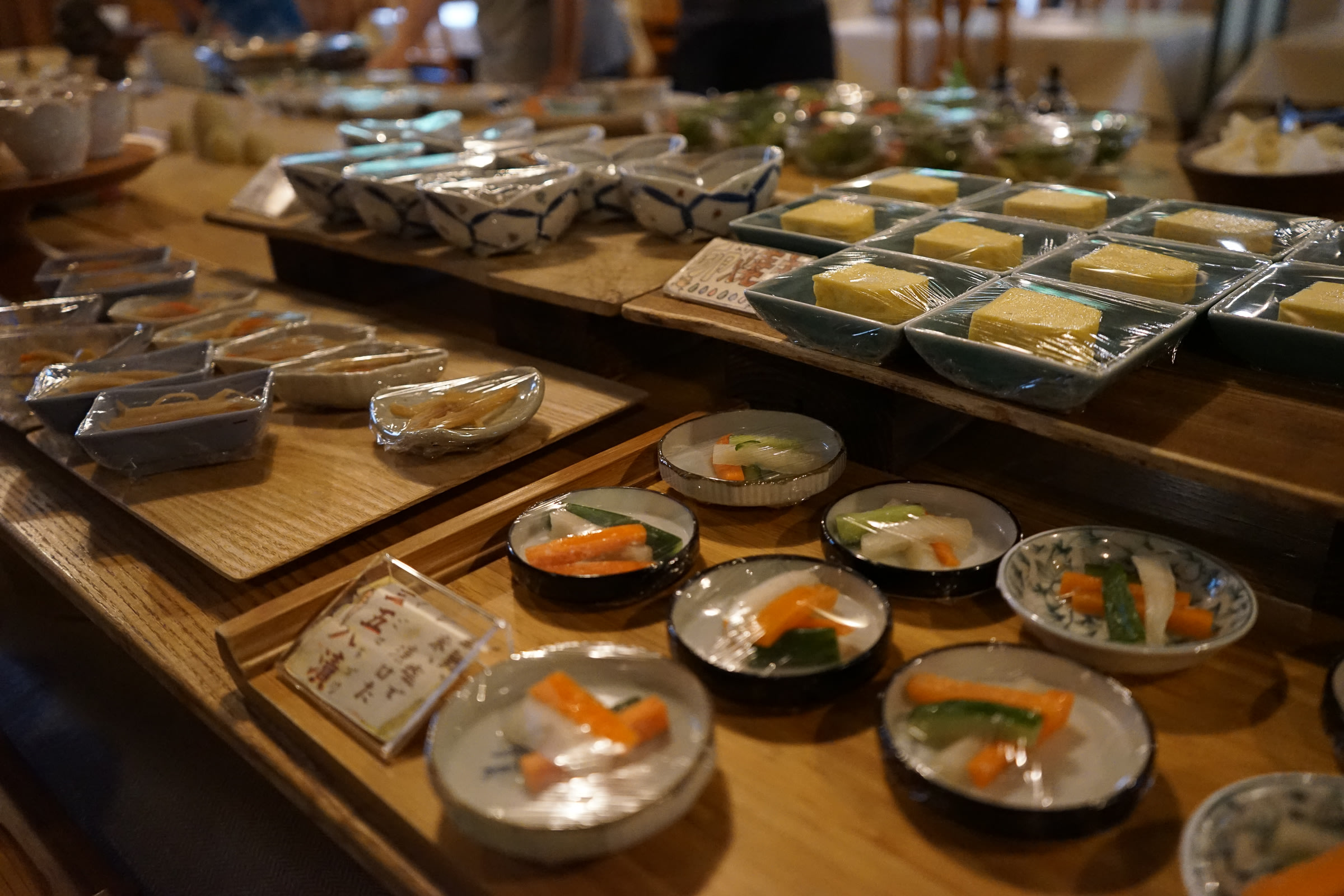 A buffet breakfast, with many small plates of food lined up on trays and tables.