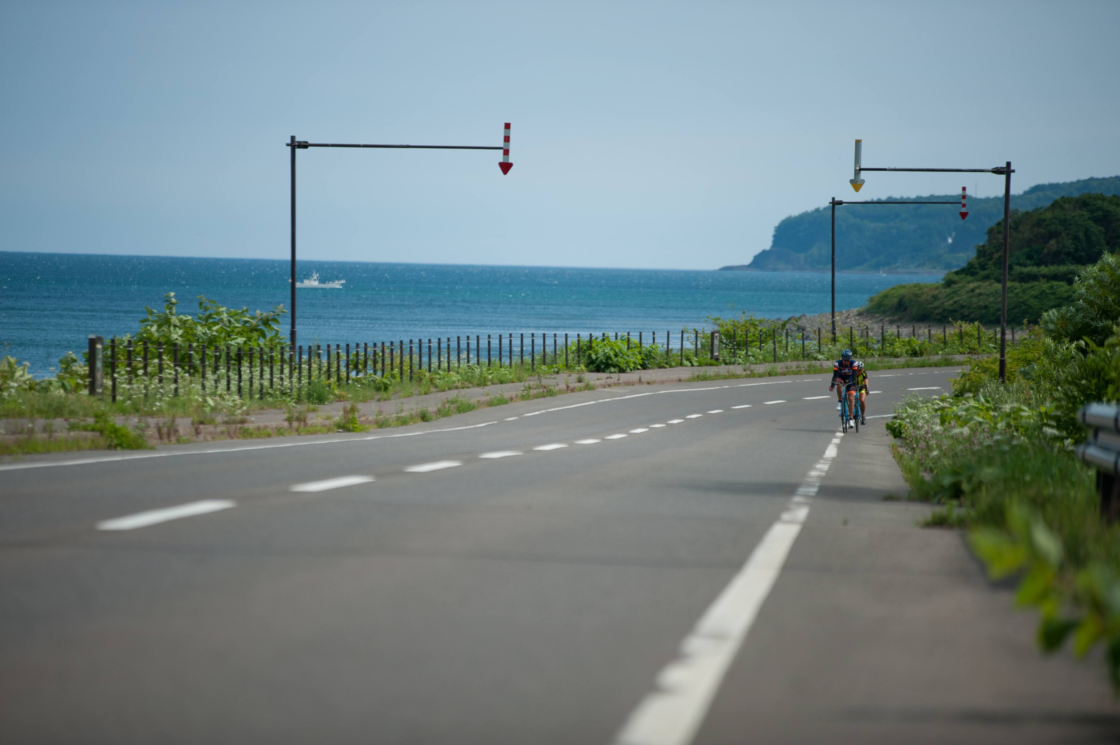Two cyclists ride along the Sea of Okhotsk coast on a clear summer day.