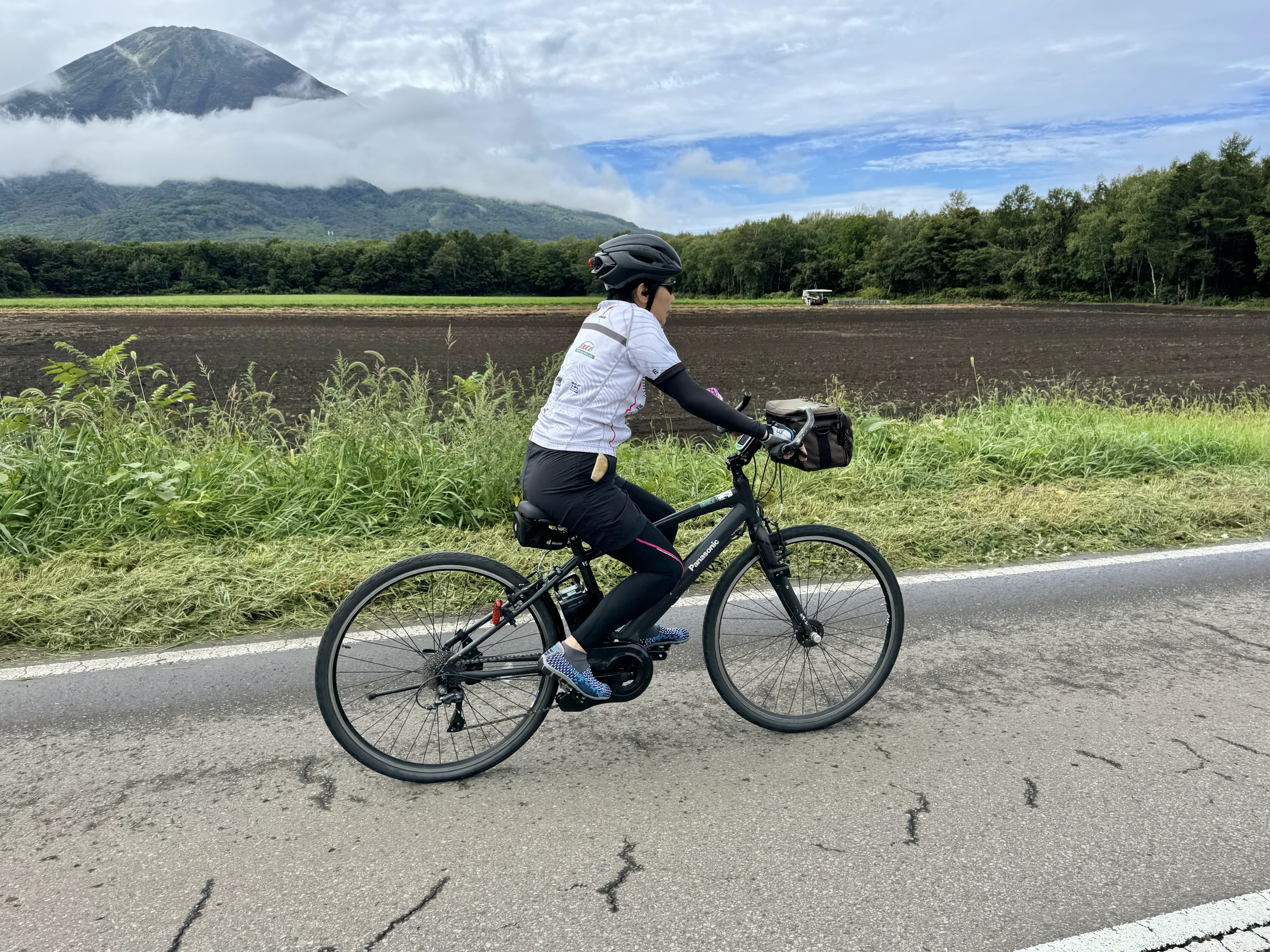 A woman cycles past Mt. Yotei, a mountain in southern Hokkaido. The mountain is partially obscured by clouds, giving it a mysterious look.