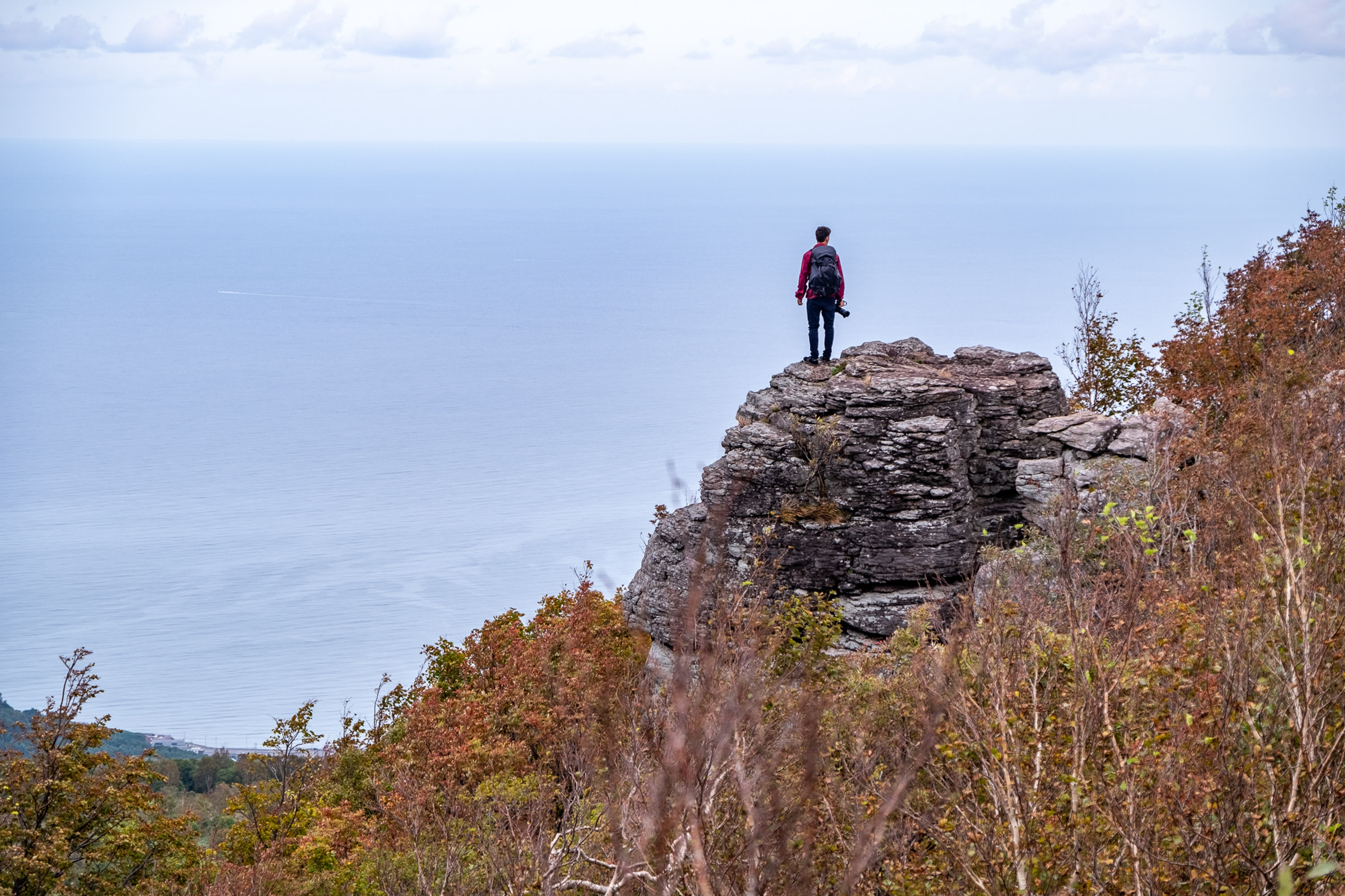 A photographer stands on a rock formation, gazing out over the ocean below.