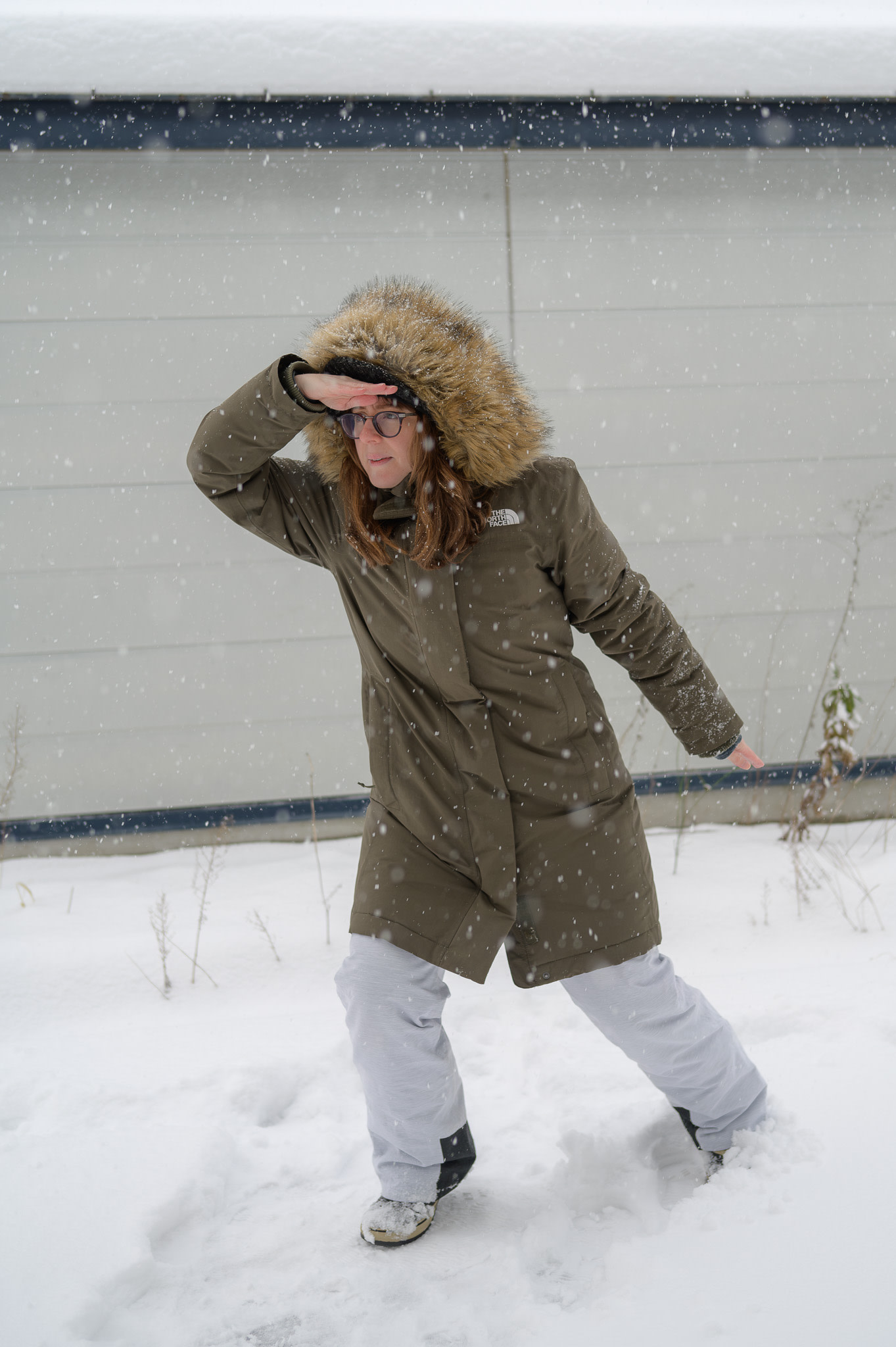 A girl stands in the snow wearing a big, warm parka with a furry hood. She is searching for animals!