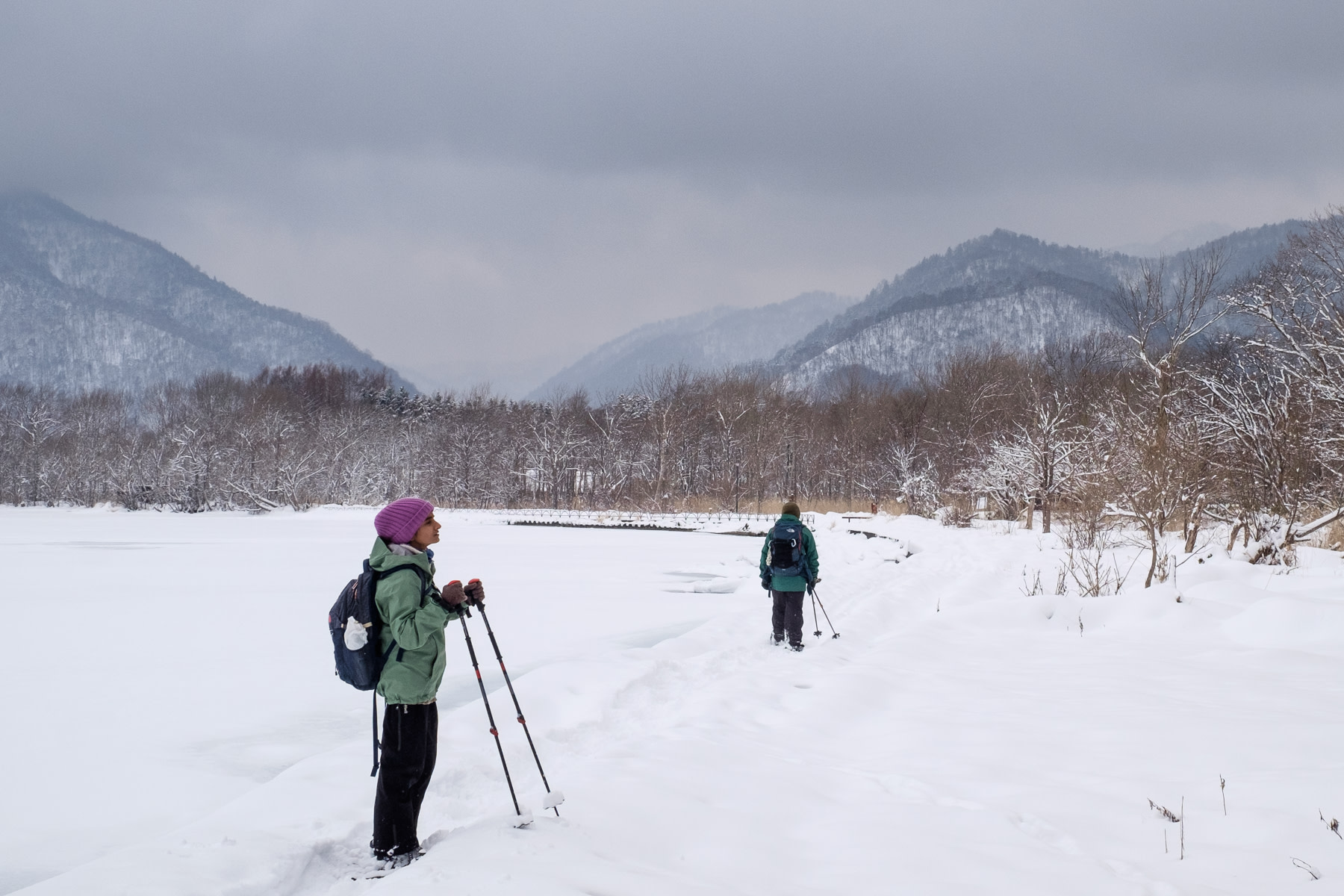 A snowshoer pauses while walking along the edge of a frozen Lake Kussharo