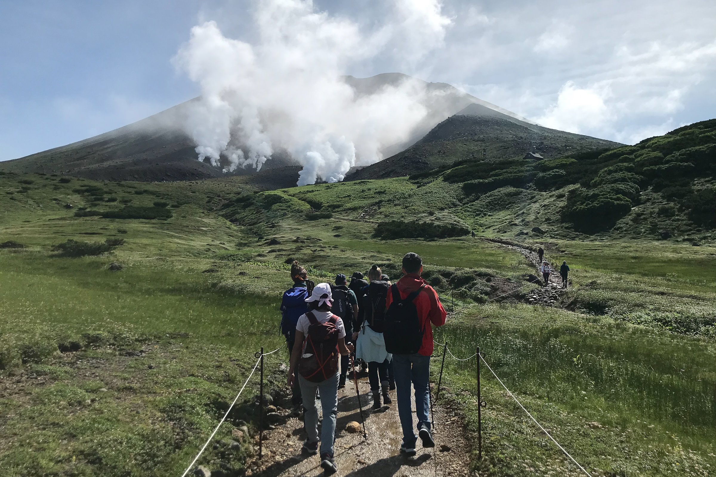 A group of hikers approach a steaming volcanic crater on Mt. Asahidake.