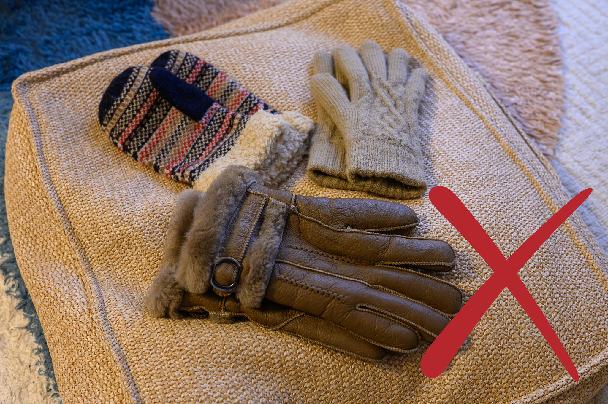 Three pairs of gloves on a cushion. One is a pair of knitted mittens, the other a pair of knitted gloves. The last pair are tan sheepskin gloves.