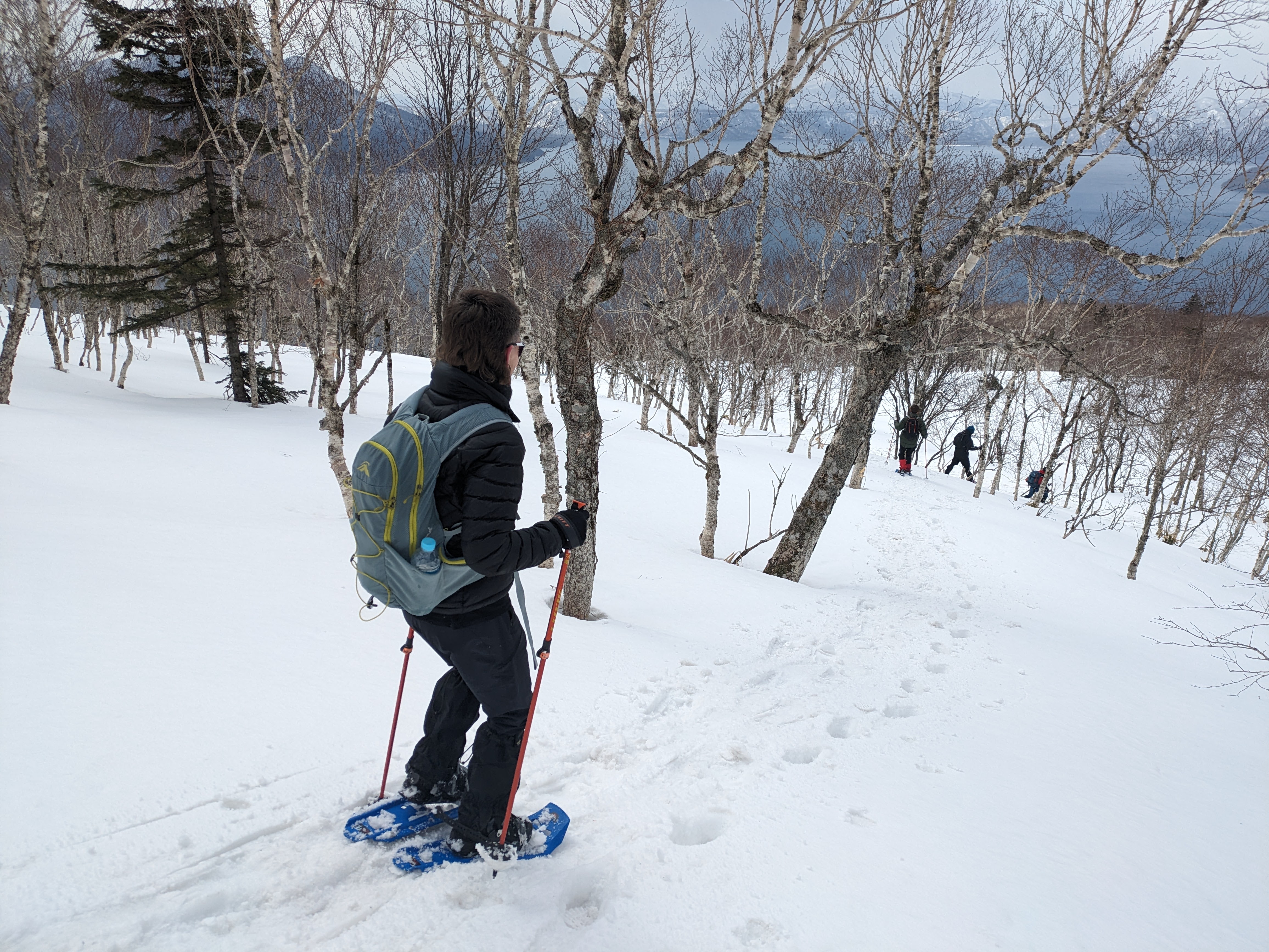 A guest descends Mt. Monbetsu on snowshoes with others ahead of her.
