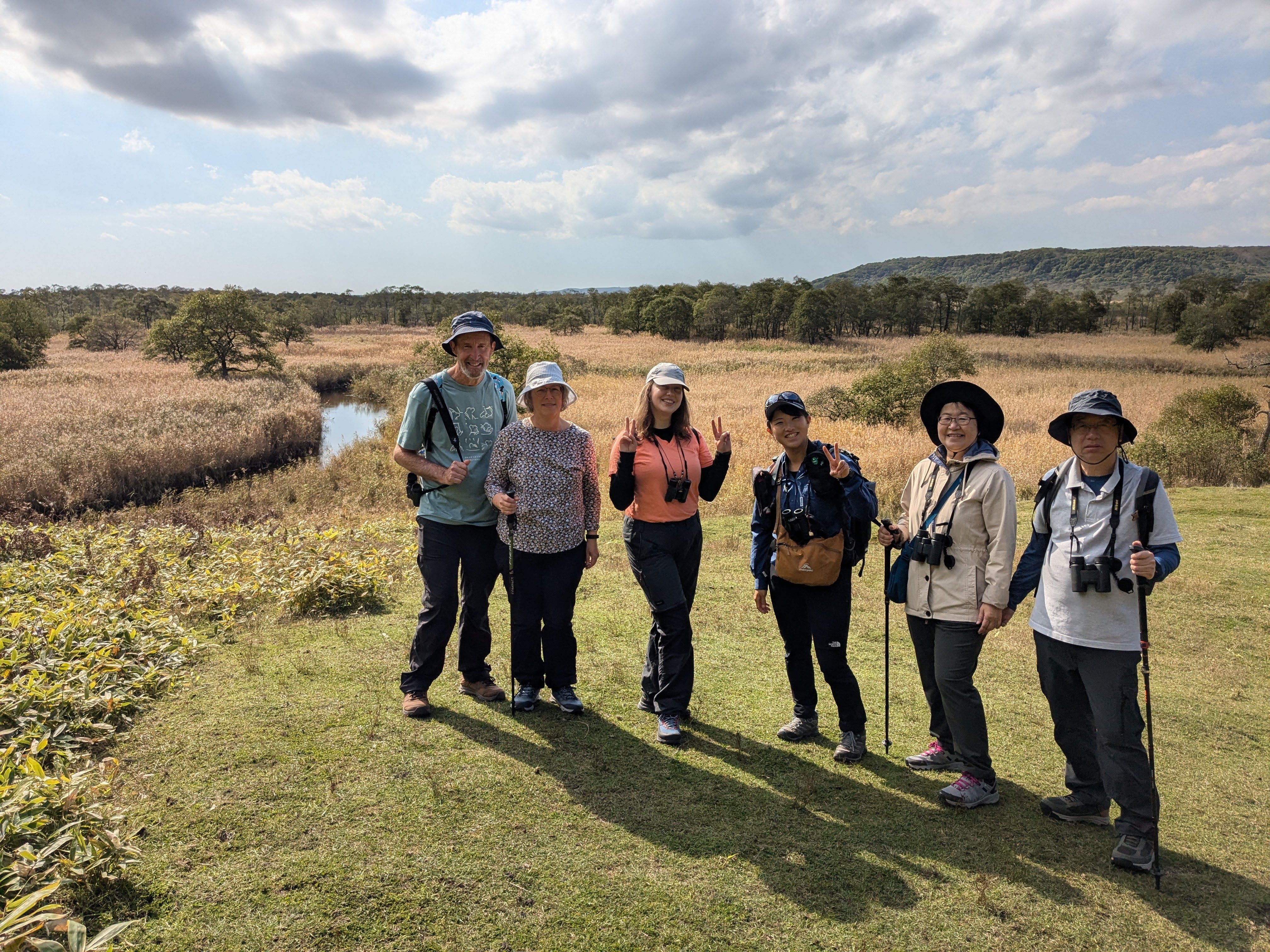 A group of six hikers in a grassland in autumn. They are all smiling at the camera.