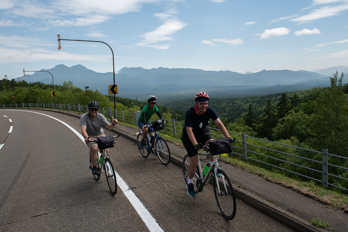 A group of cyclists ride past mountain scenery in the Daisetsuzan National Park