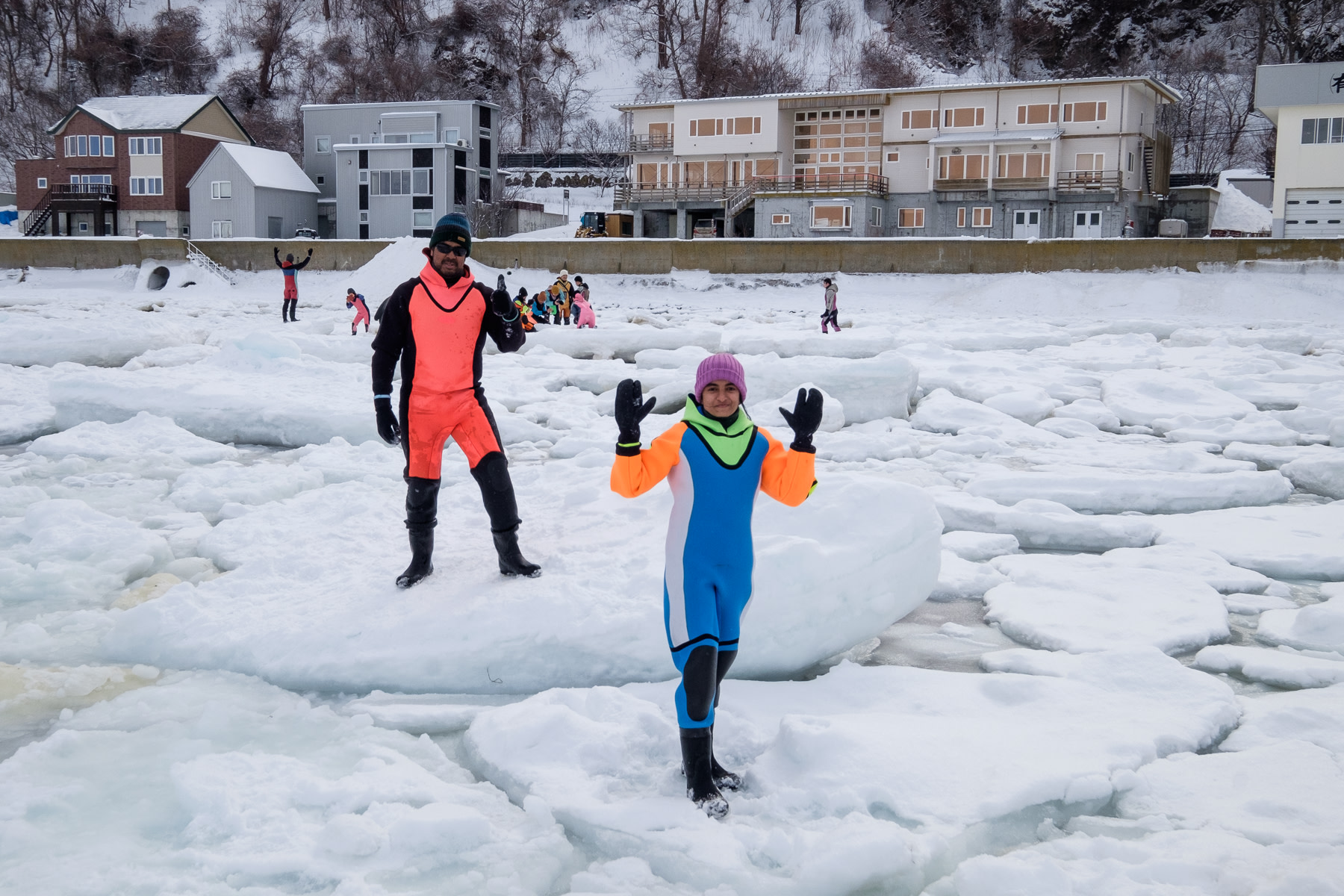 Two tourists wearing dry suites pose for a photo while standing on drift ice off the coast of the Shiretoko Peninsula