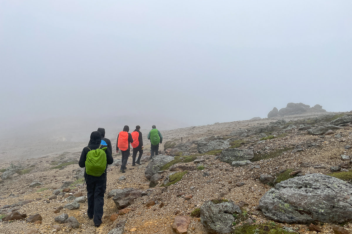 Hikers walk through the fog in a barren alpine landscape