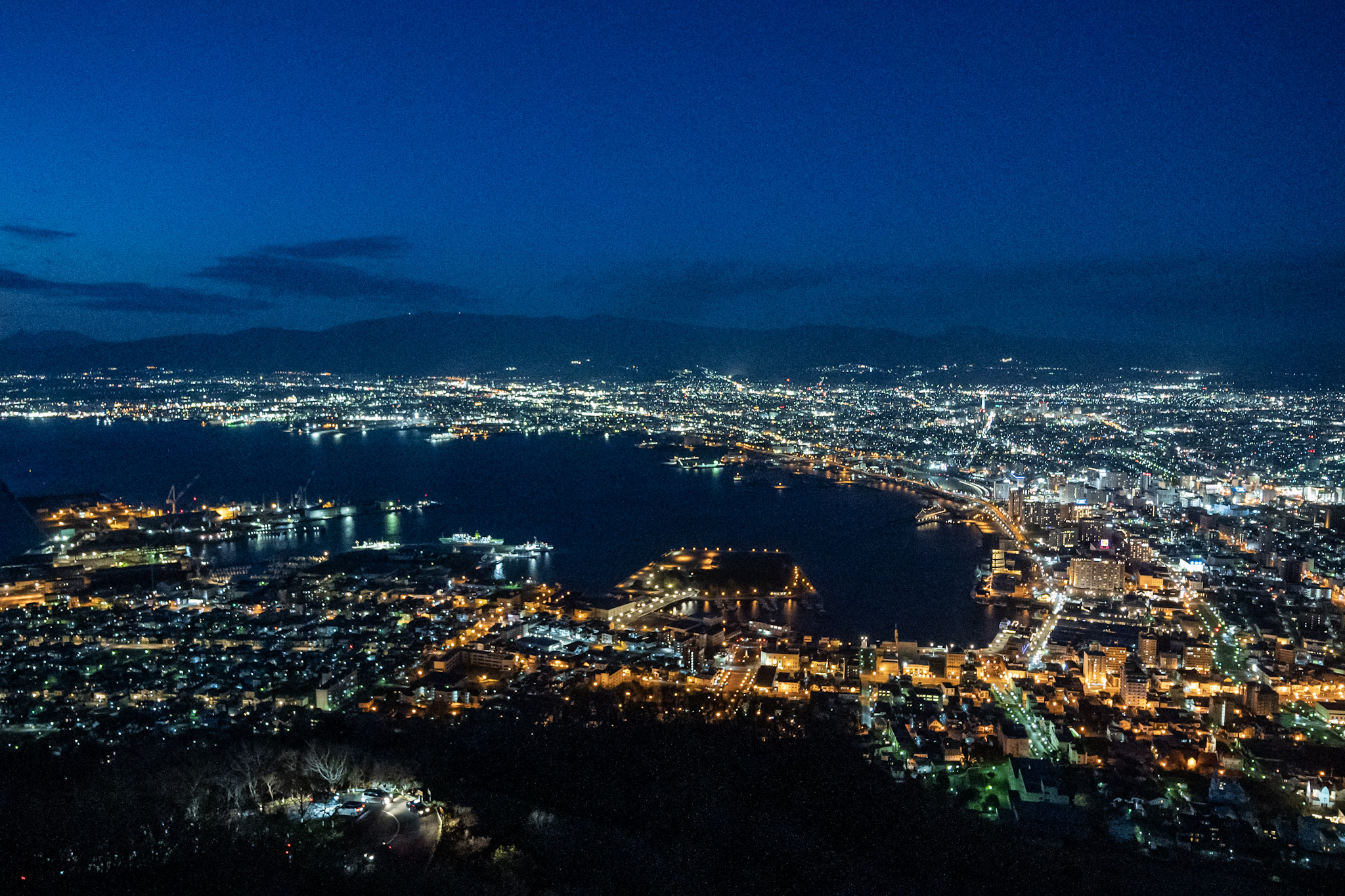 Hakodate's famlous night view. It is dark, save the view of the city illumination in the distance below. The shape of Hakodate Bay is clearly visible with the arc of the lights.