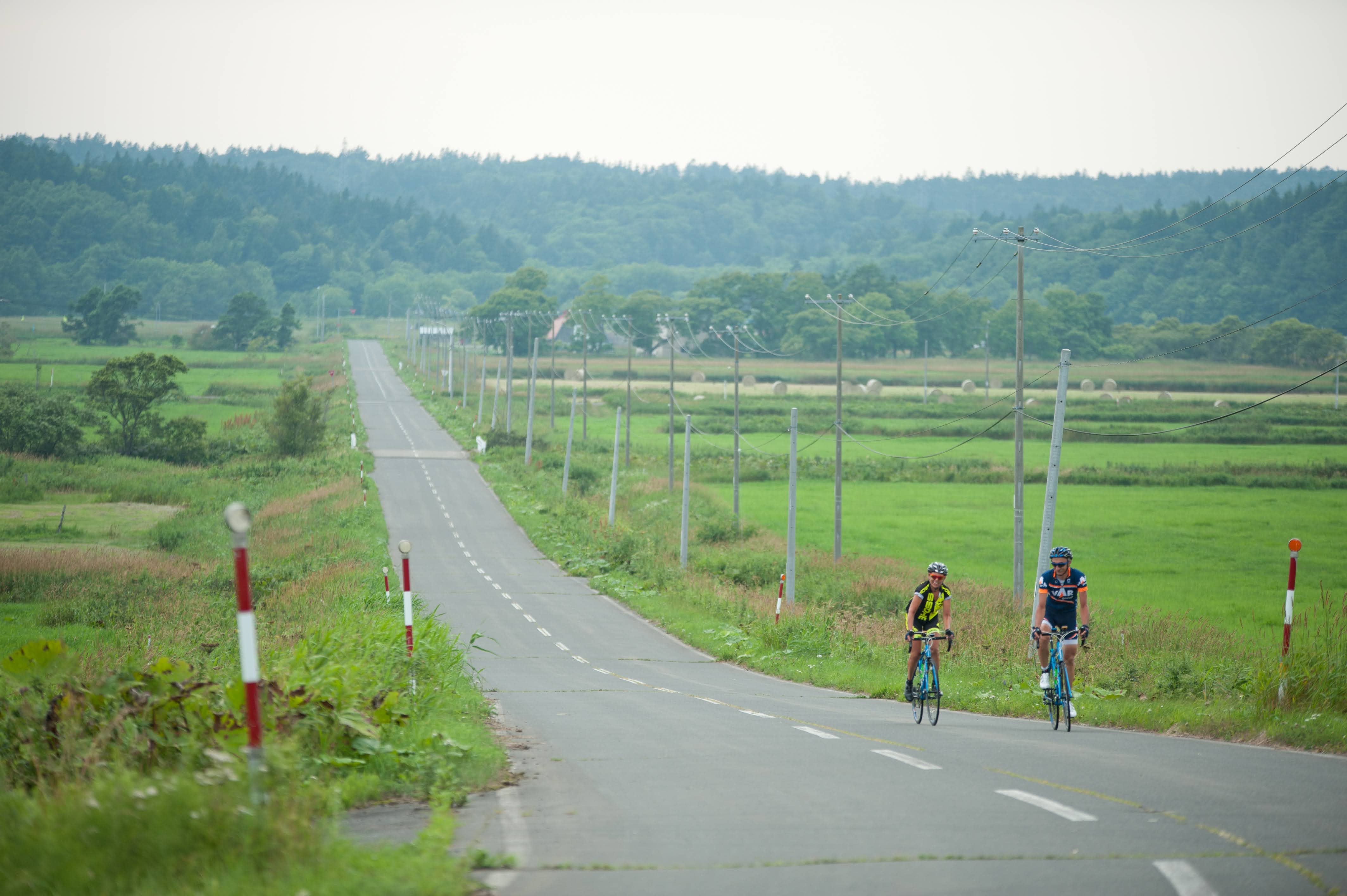 Two cyclists ride down an empty country road in the Nakashibetsu area.