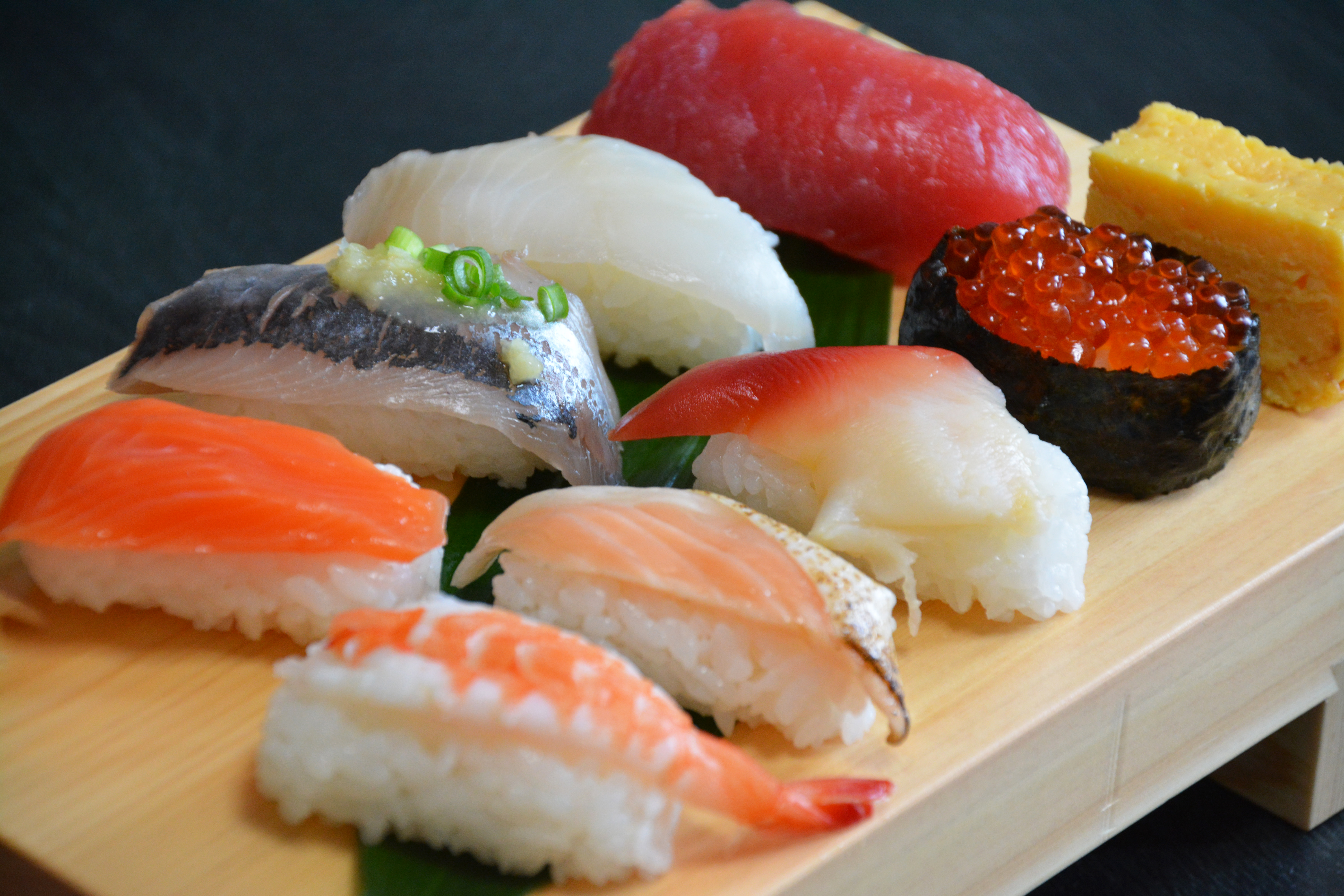 A traditional wooden platter of colourful nigiri sushi (small balls of rice topped with slices of raw fish).