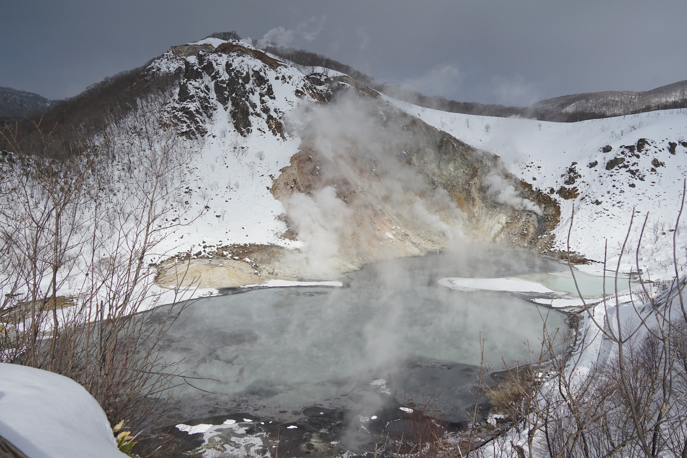 Steaming Oyunuma hot pond surrounded by snow-covered hills.