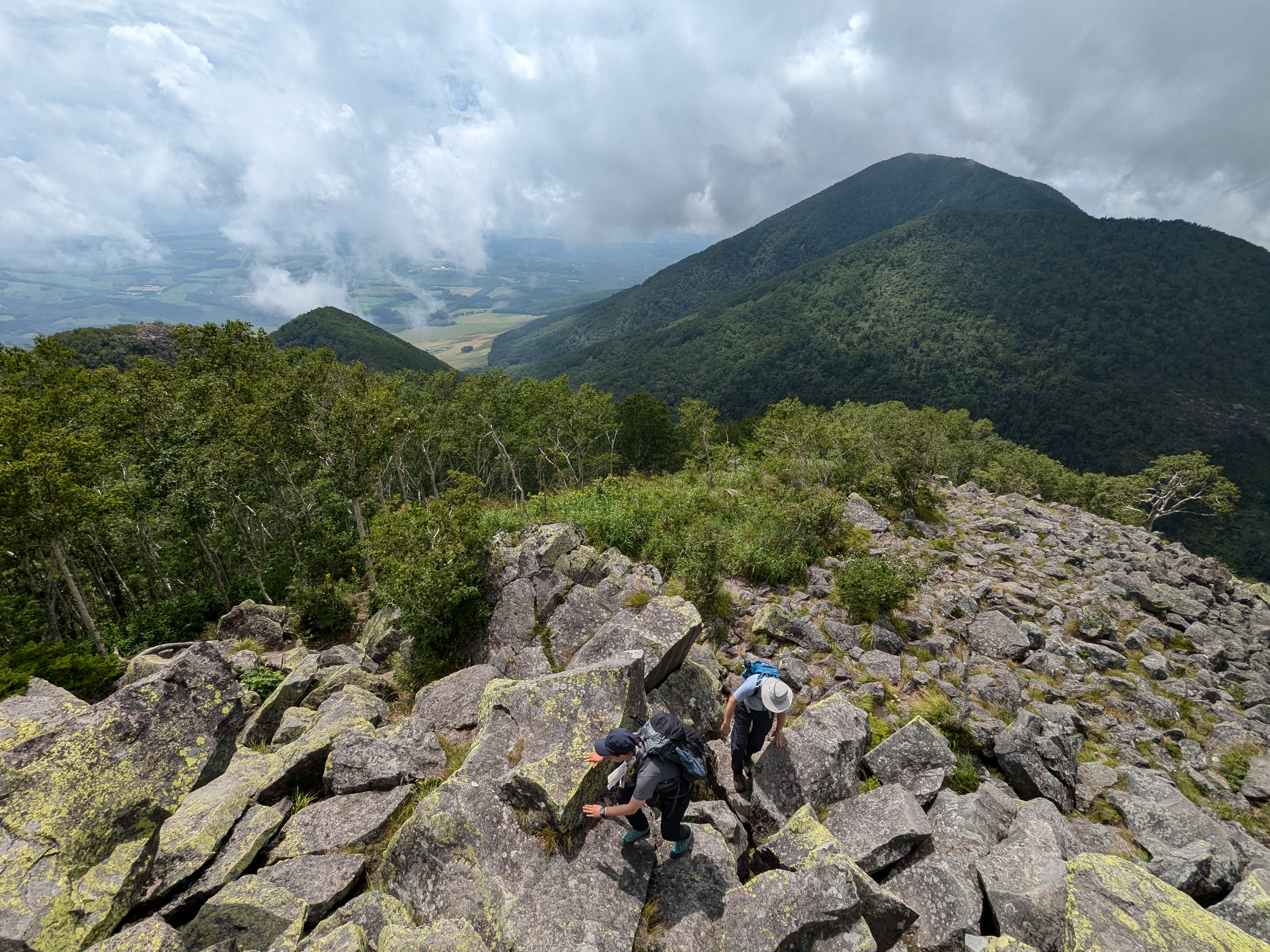 Two hikers scramble up a rock field near the summit of Mt. Hakuunzan in Daisetsuzan National Park