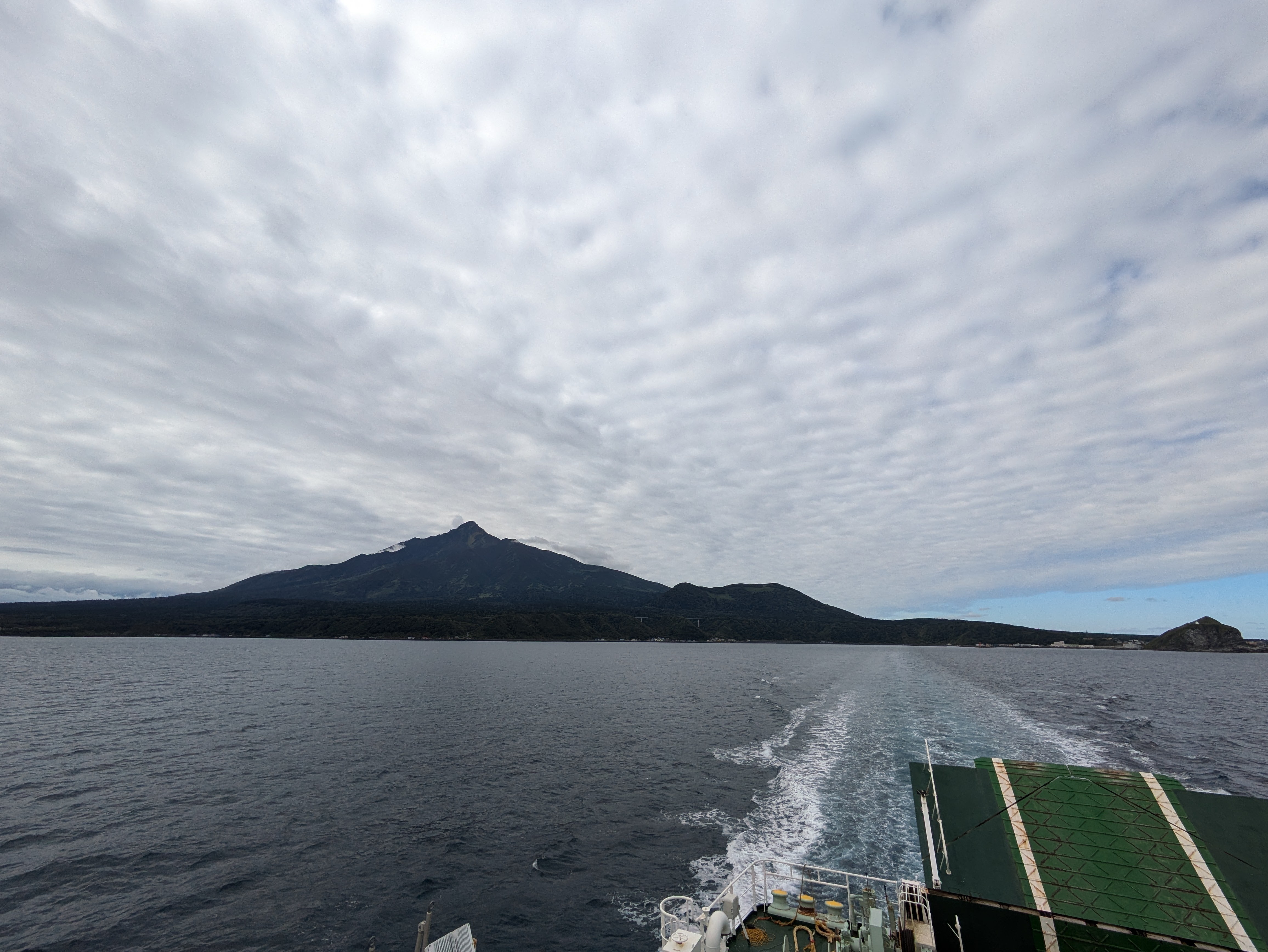 A ferry makes its way across the ocean, sailing away from Rishiri Island, visible in the distance.