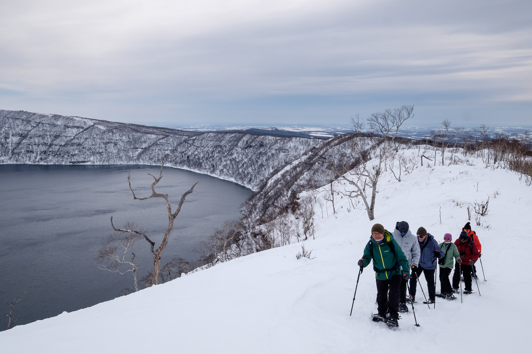 A guide leads a group of snowshoers along the edge of the Lake Mashu crater