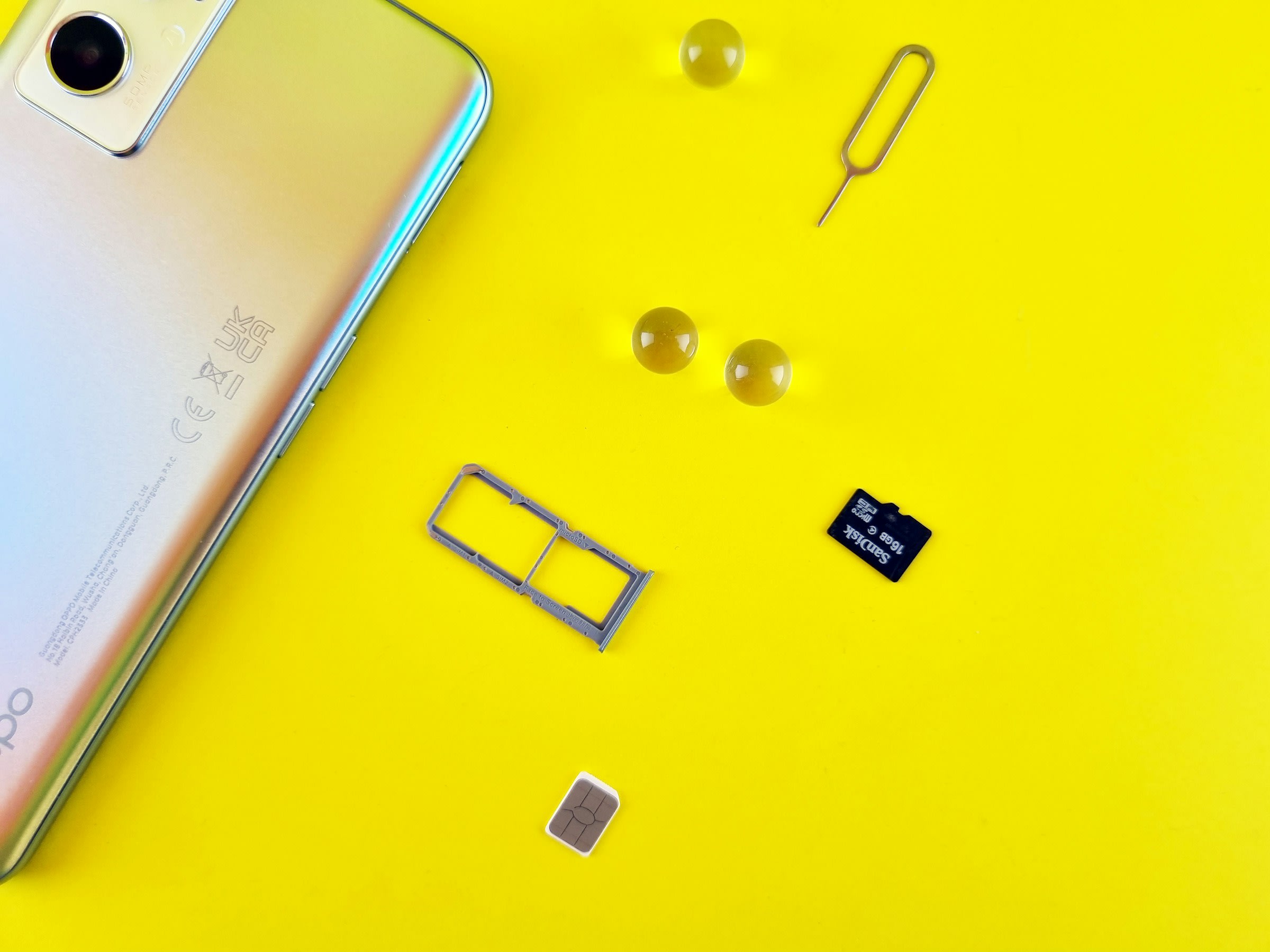 A smartphone with its SIM card tray open, the SIM card laid out on a yellow surface.