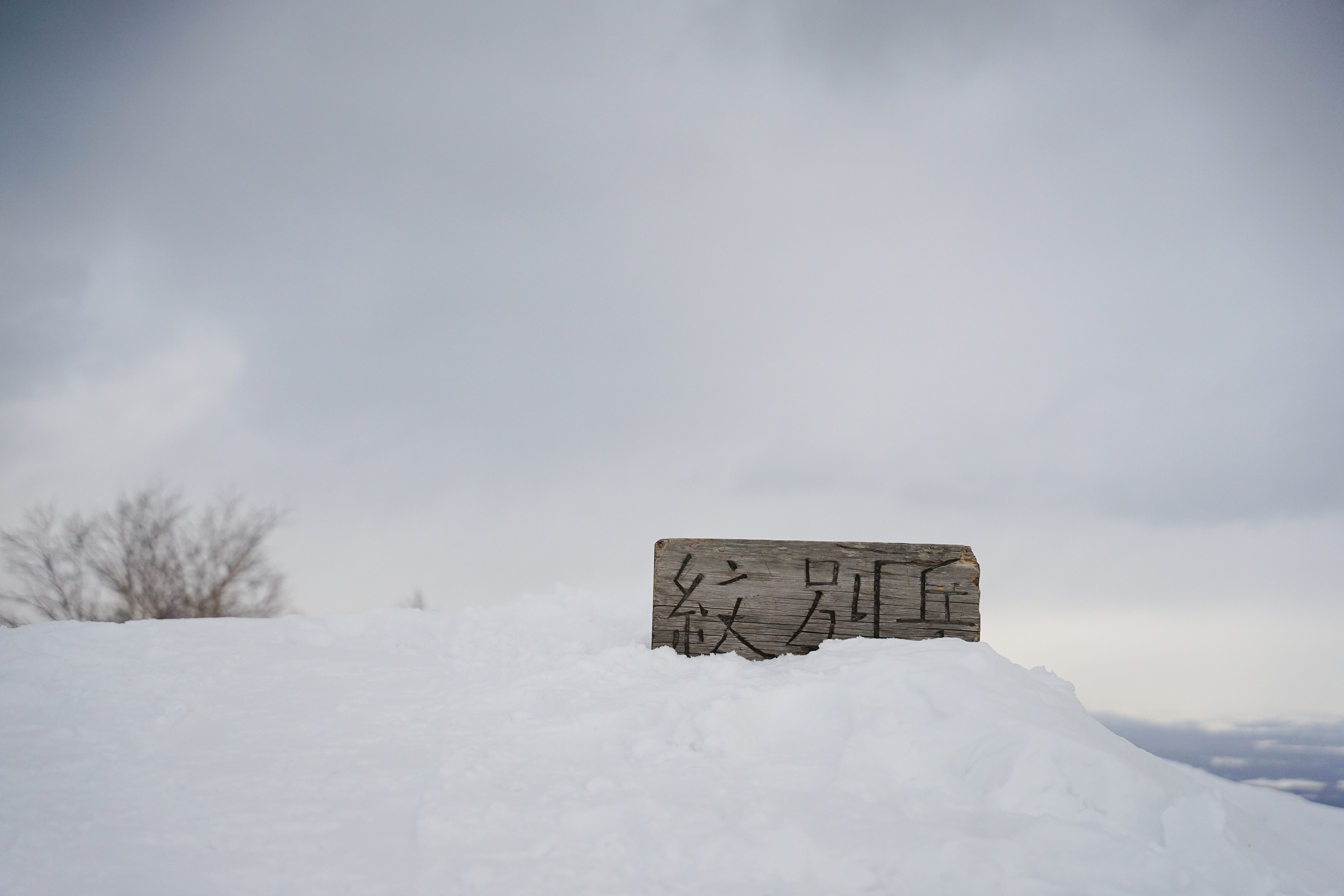 The summit signpost of Mt. Monbetsu half-buried in snow.