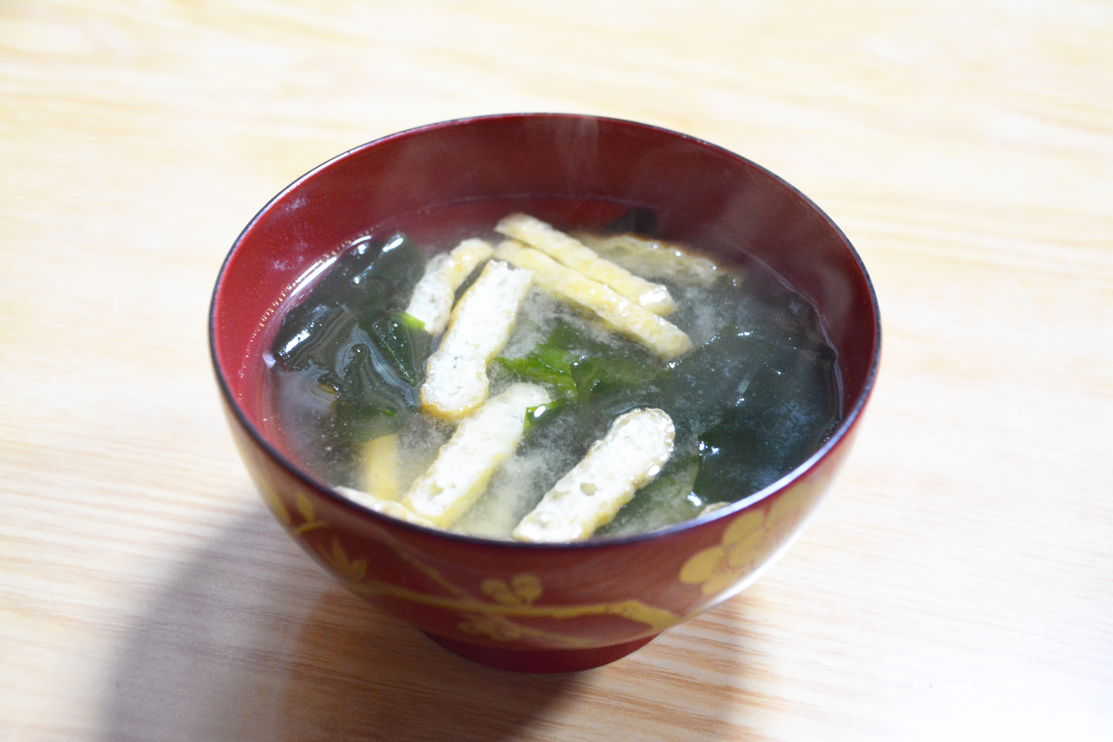 A bowl of miso soup on a table. In the soup are thinly-sliced pieces of tofu and kelp.