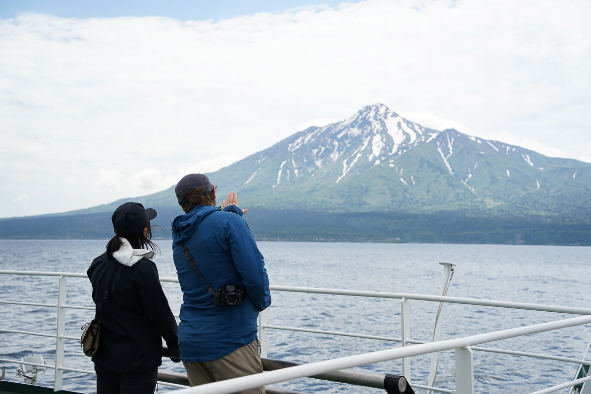 Two guides talk about climbing Mt Rishiri whilst looking back at the mountain from a ferry