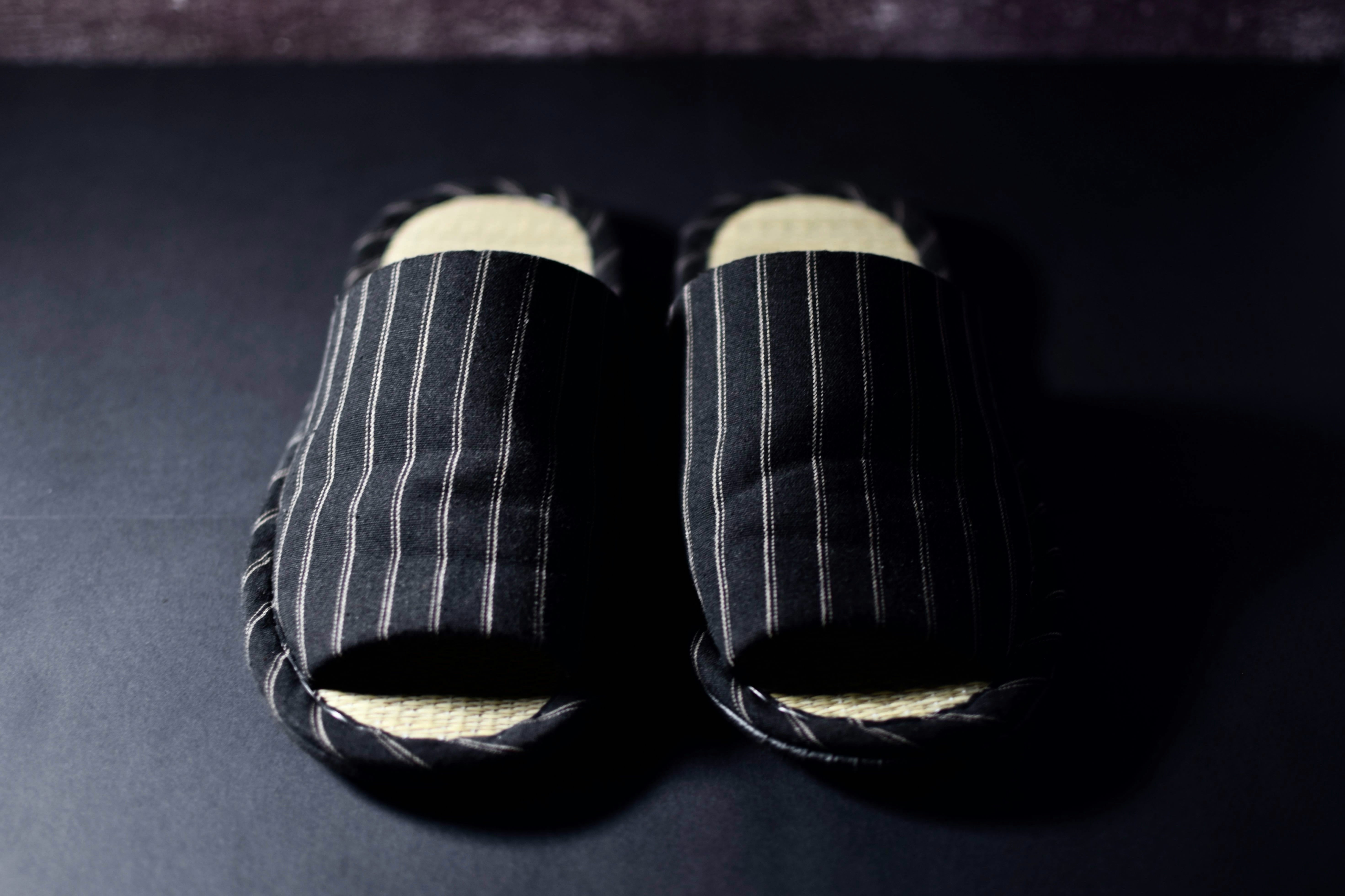 A pair of fabric slippers placed on a dark, smooth floor.