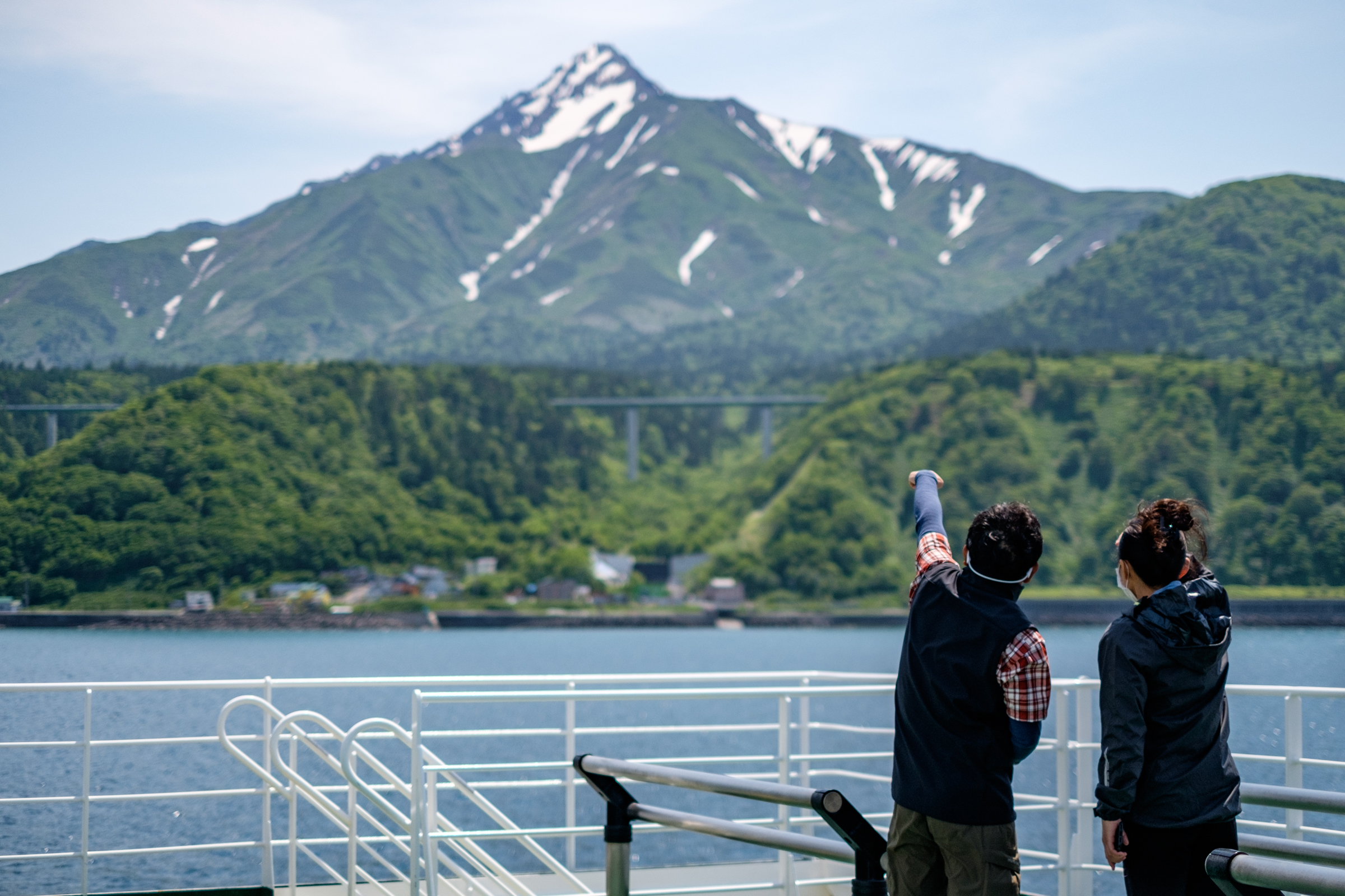 A nature guide points to the summit of Mt Rishiri, which still has a few remaining snow patches, from the ferry between Wakkanai and Rishiri.