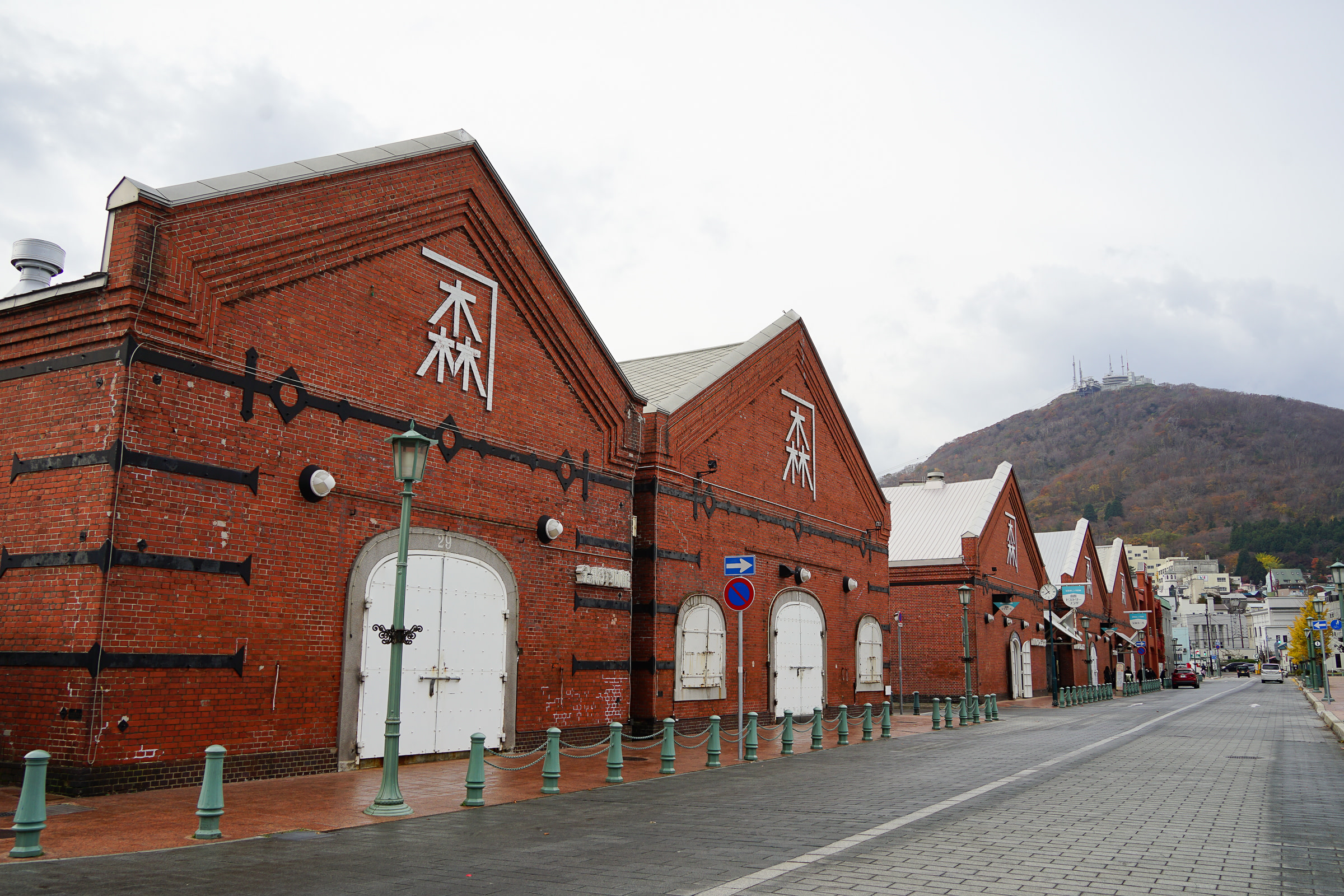 Red brick warehouses in Hakodate. Several of them line a cobblestone street.