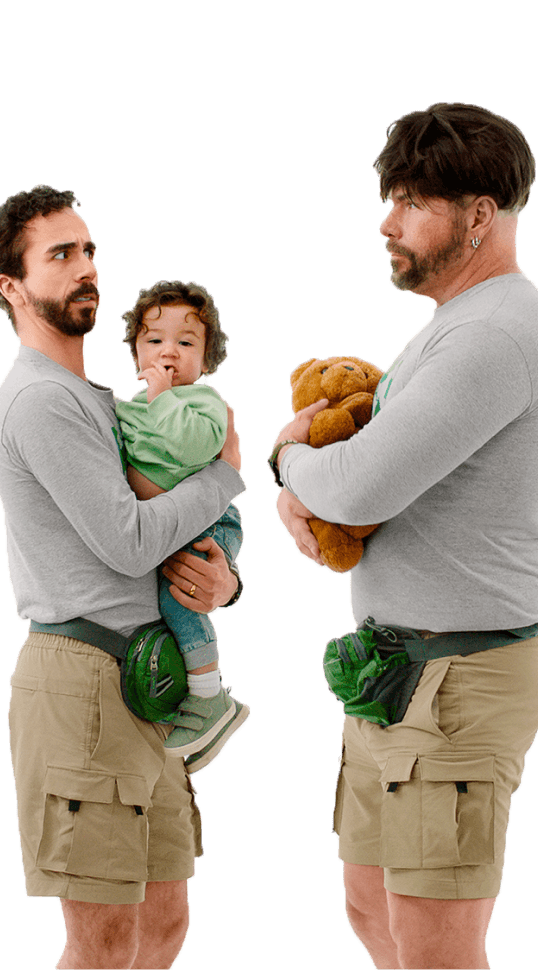 A man, holding a baby, looks suspiciously at an unconvincing impostor: a man who’s dressed just like him, wearing a wig and holding a teddy bear.