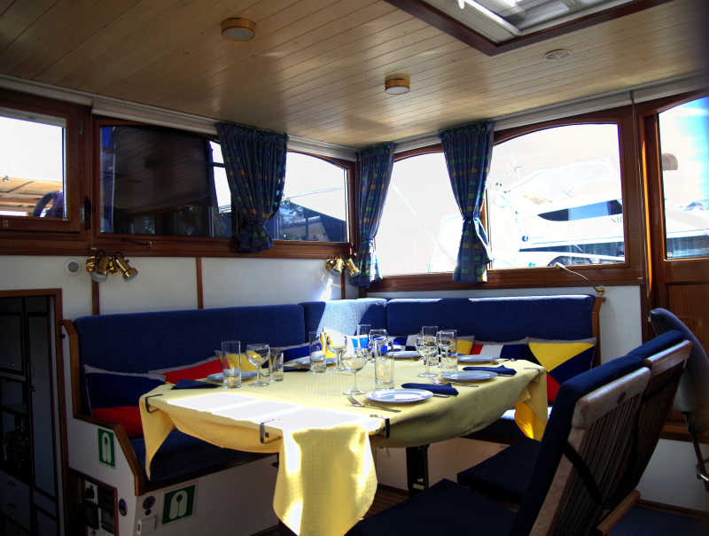 Salon mit blauen Bänken und Esstisch auf der Yacht Löcknitz