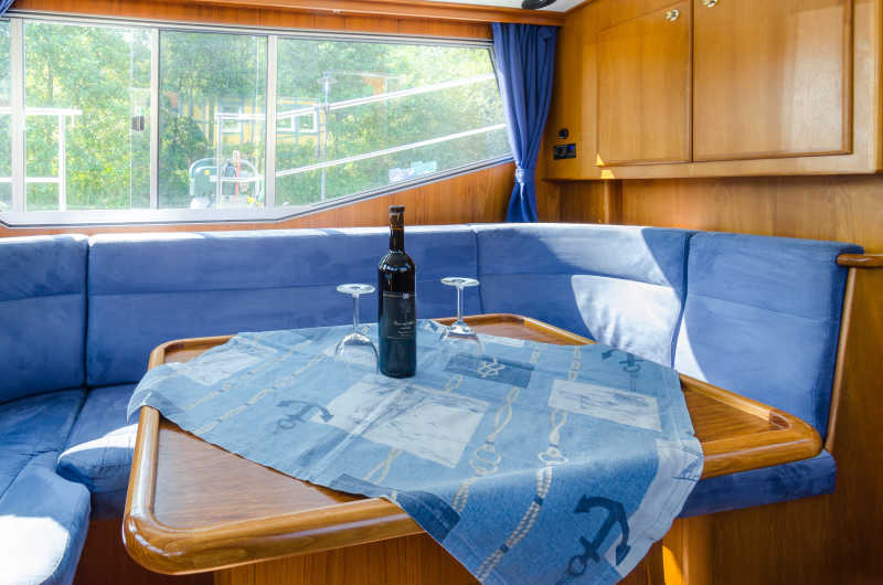 Sitzecke und Tisch aus Holz und mit blauen Kissen auf dem Hausboot Carlotta