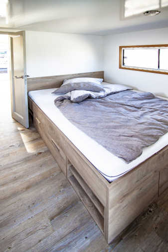 Schlafzimmer mit Bett und Holzfußboden auf dem Hausboot Flexmobil