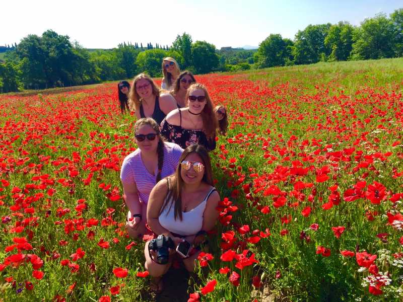 8 female students standing zigzag in a field of red poppies.