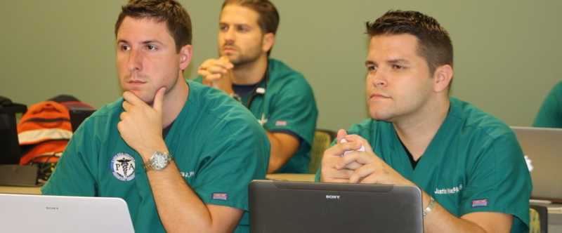 Photograph of Three Male PA Students in the LEC Classroom with laptops in front of them. 
