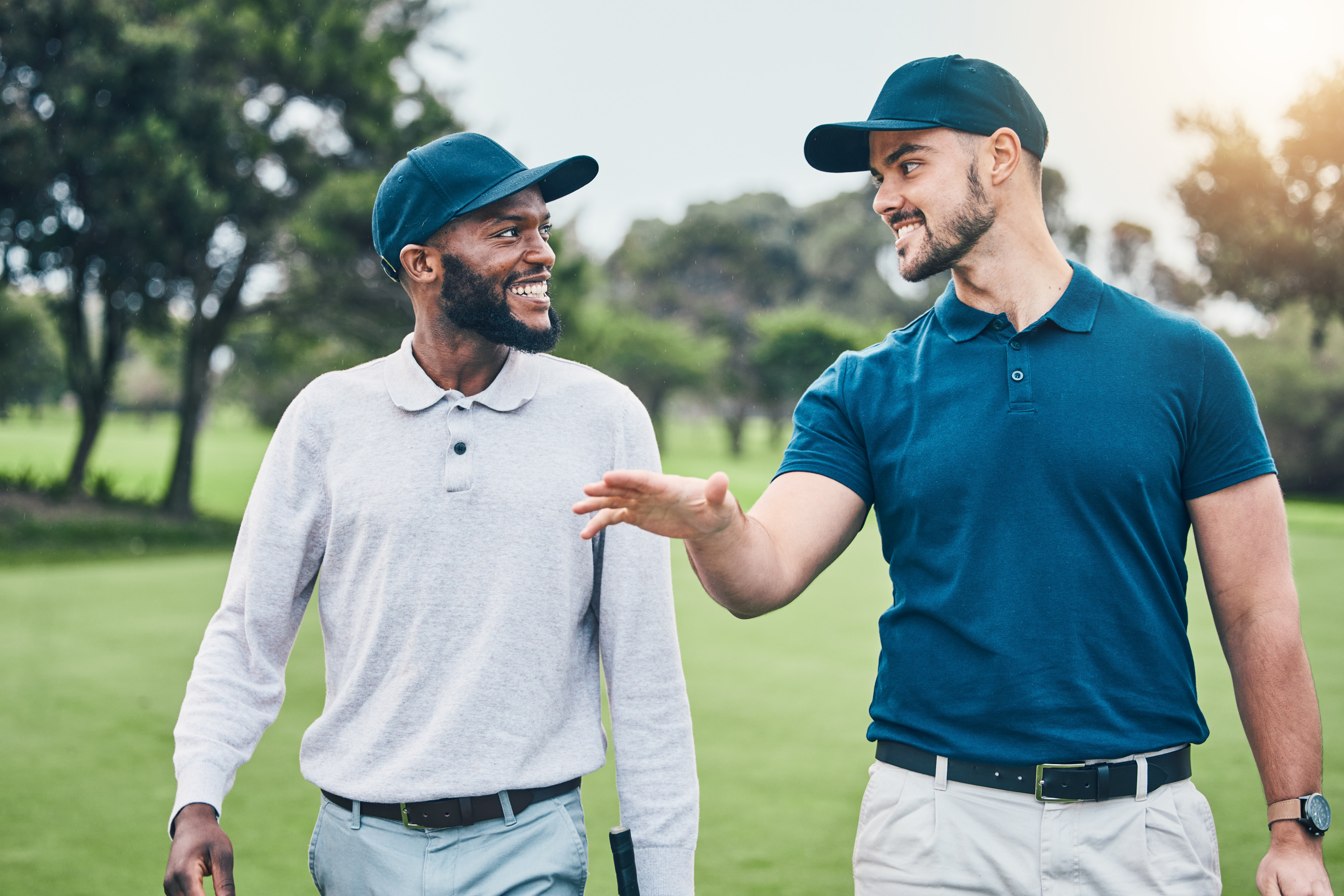 Two men walking with golf clubs, laughing. 