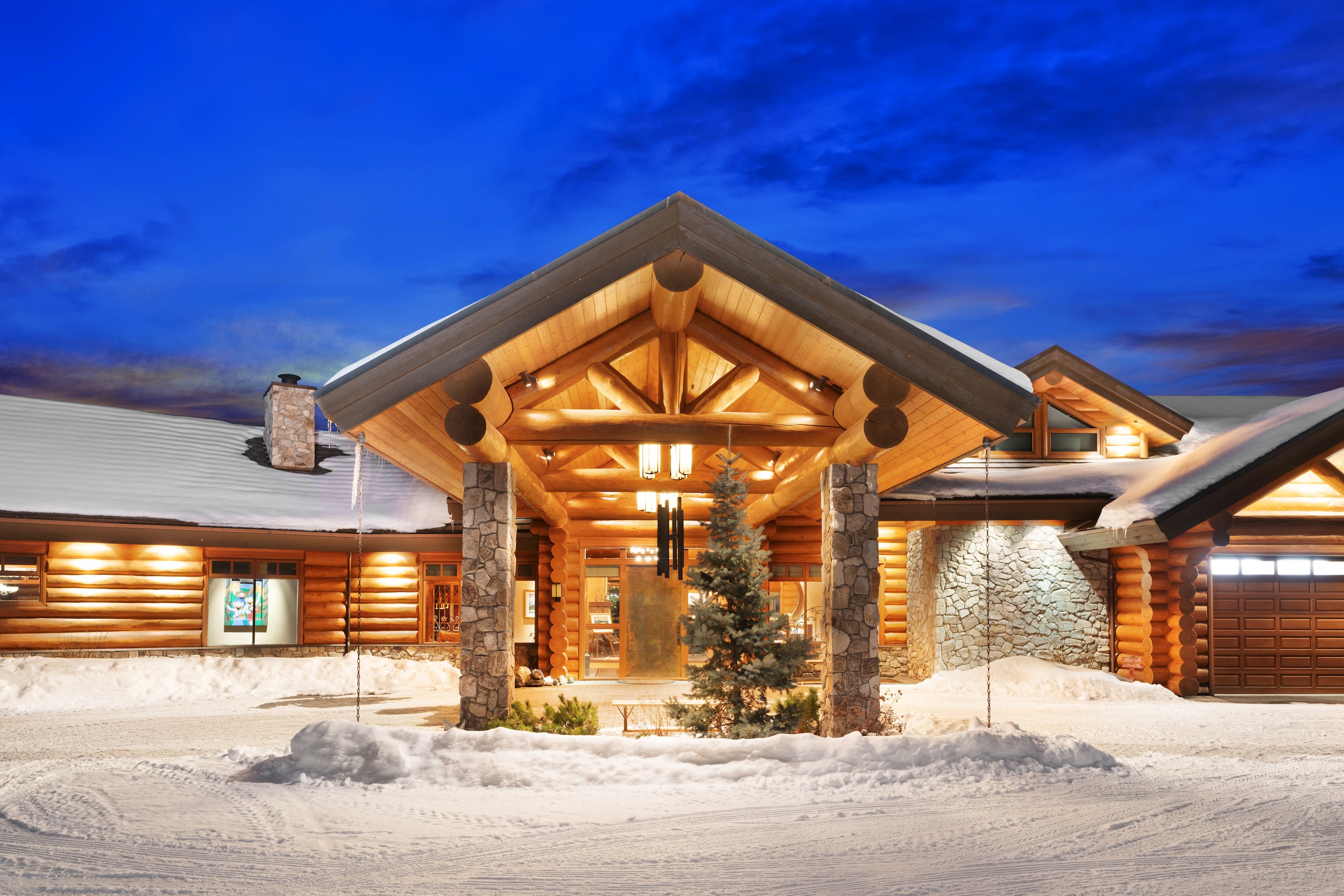 Front entrance of log cabin with snow on ground.