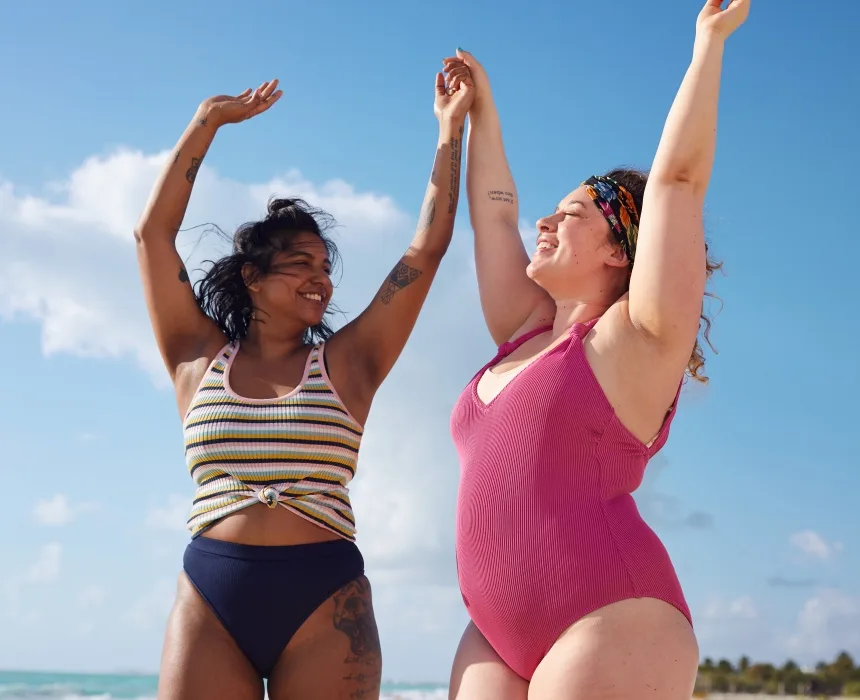 Two women jumping at the beach, one is bigger than the other