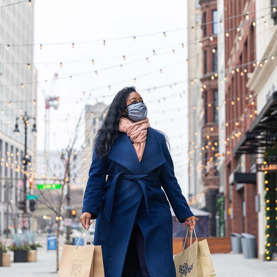 masked woman walking downtown with shopping bags