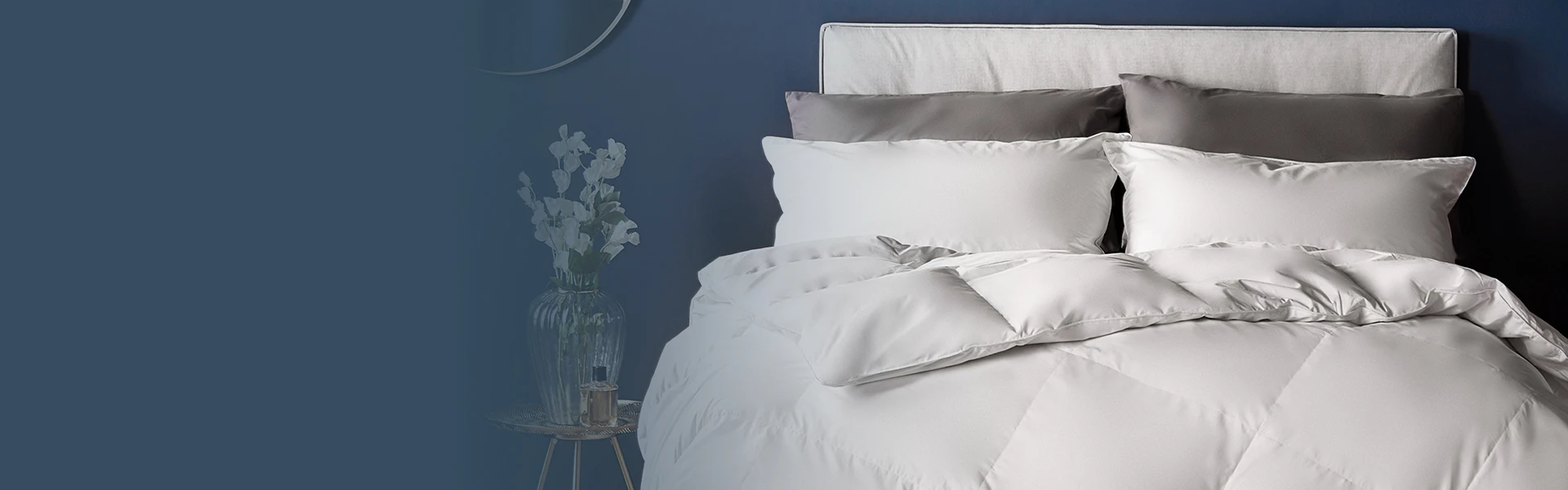feather pillows & duvet on bed. Flowers in vase next to bed