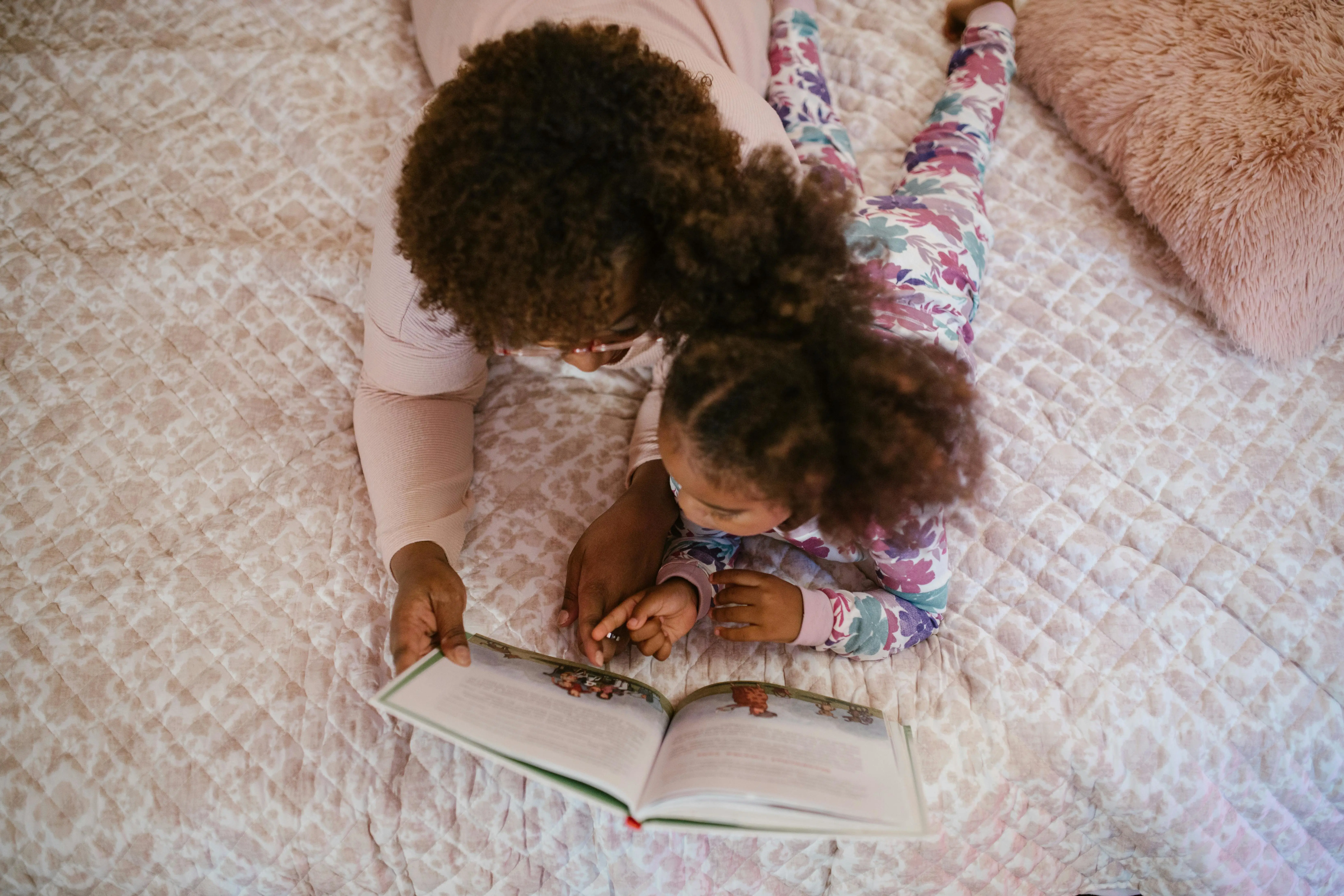 A young child and their mother lay on a bed reading a book as part of a back to school sleep routine