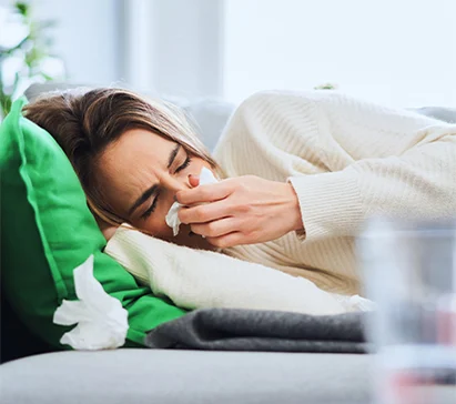 Woman lying down, blowing her nose, surrounded by tissues