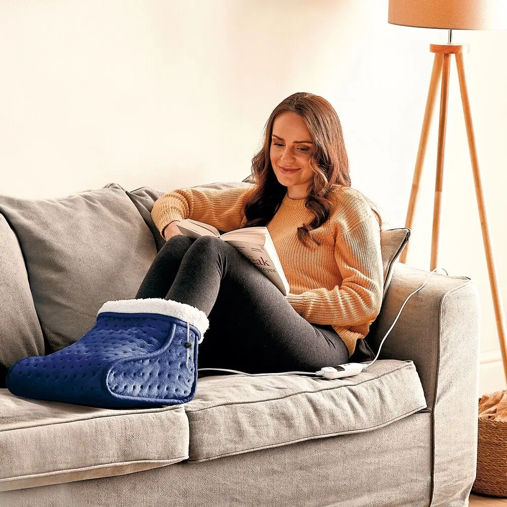 a woman sat on a sofa reading a book with her feet in a navy blue foot warmer