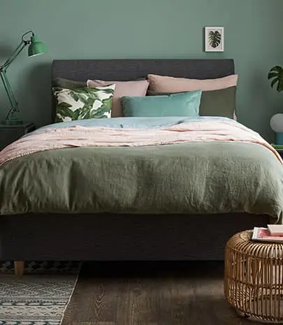A tidy green bedroom with plants, divan, nightstand, bedding and accessories.