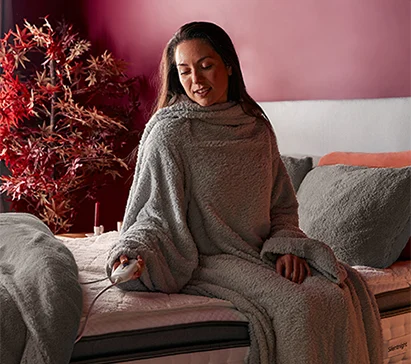 Woman sat on a bed wrapped in a Snugsie wearable blanket