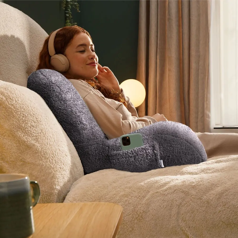 A woman wearing headphones leaning back into a Silentnight cuddle cushion 