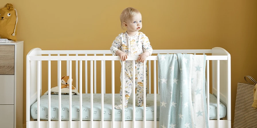 Baby stood in a cot with blanket