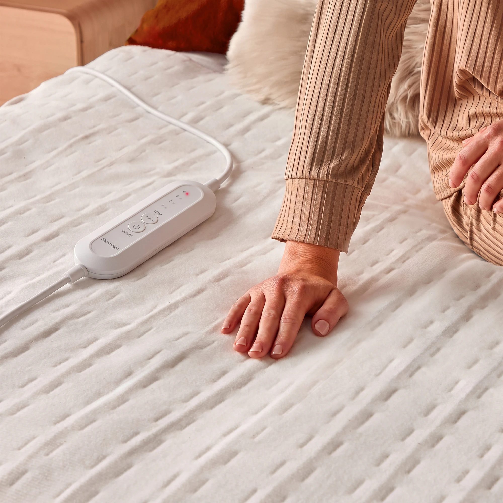 A hand touching the top of an electric blanket, next to the blanket's control switch