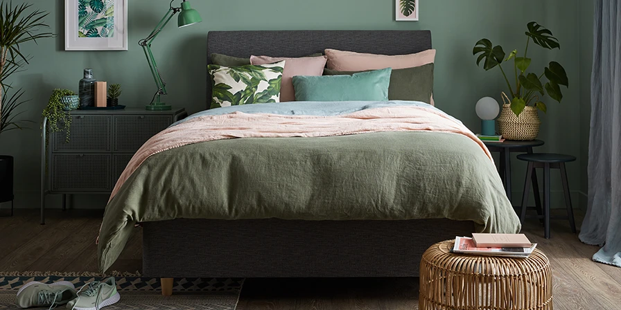 A tidy green bedroom with plants, divan, nightstand, bedding and accessories.