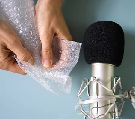 Hands popping bubble wrap next to a microphone